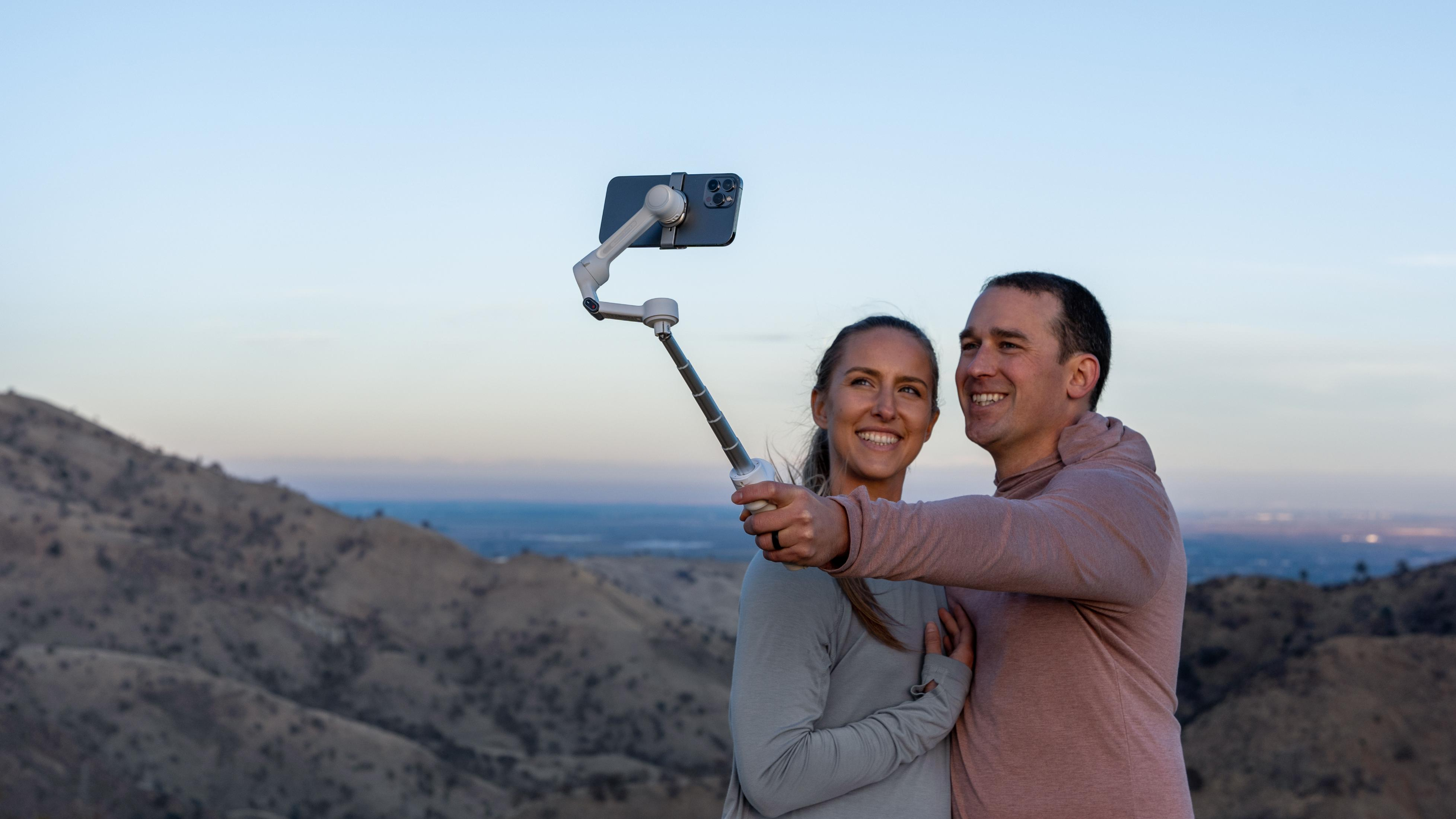 Ein Paar macht ein Selfie mit einem Gimbal auf einem Hügel.