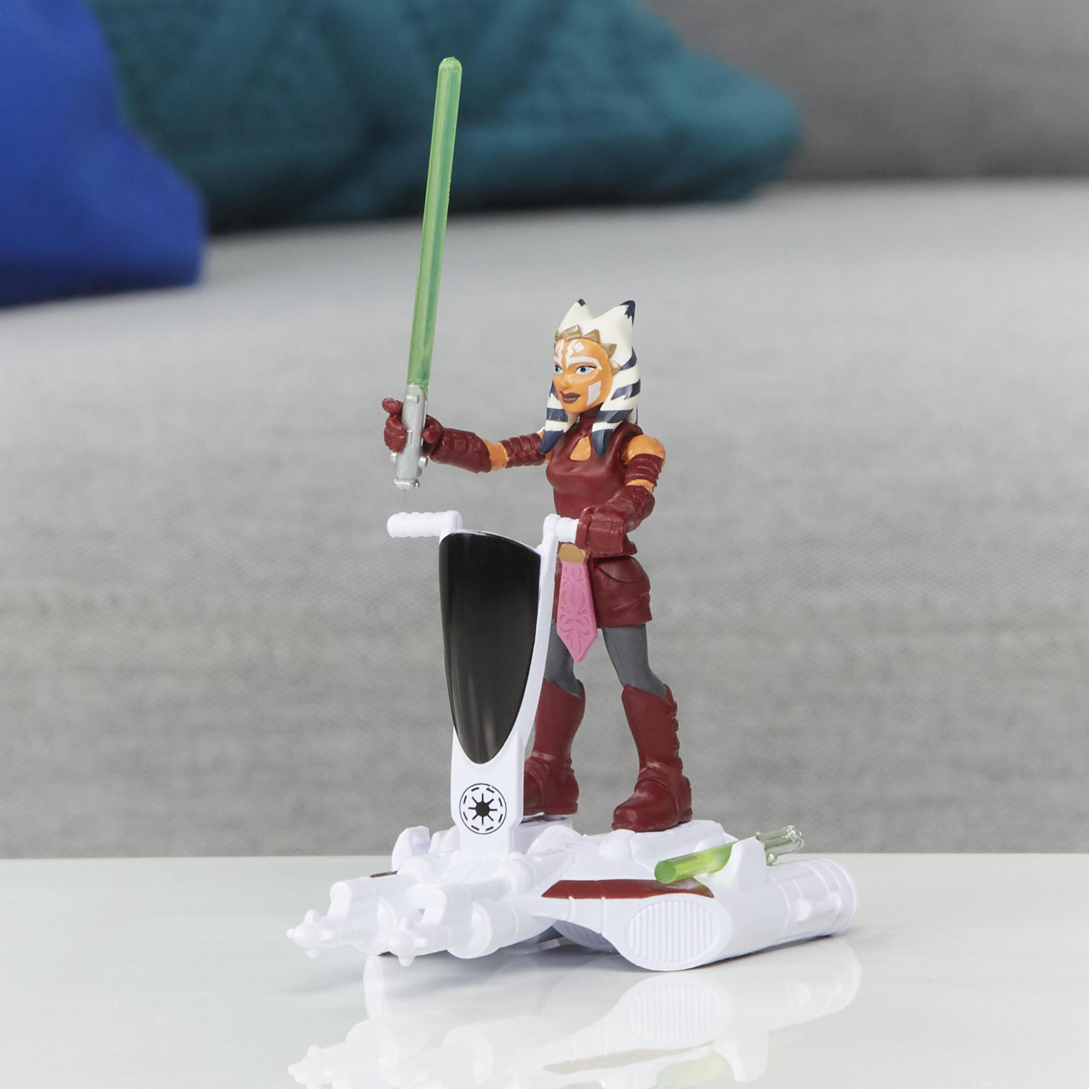 Figura de acción de Ahsoka Tano con sable de luz en un vehículo blanco con emblema galáctico.