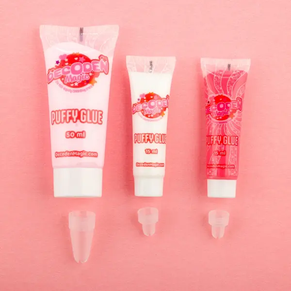 Tres tubos de Decoden Magic Puffy Glue en rosa y blanco sobre fondo rosa.