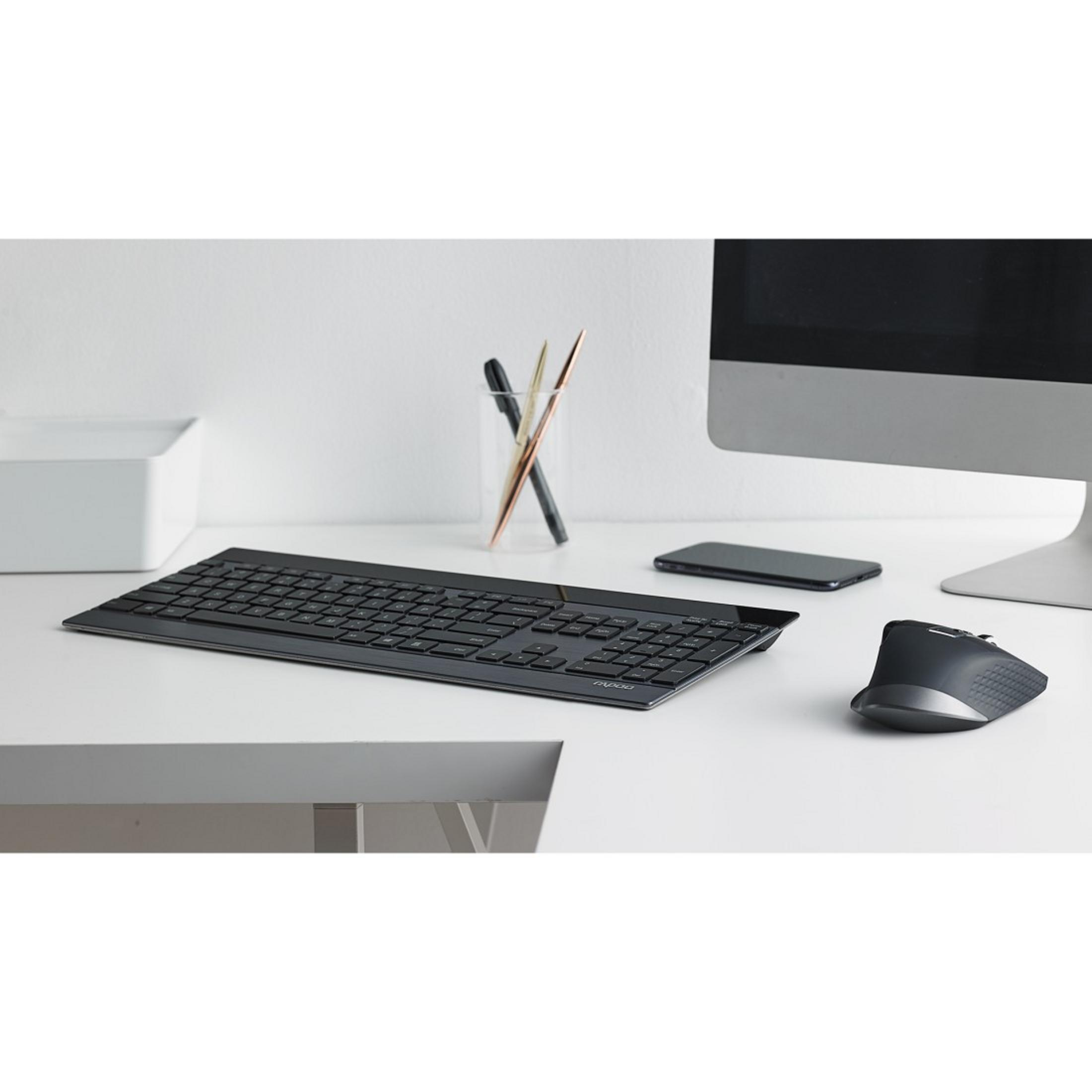 Schwarze Tastatur, Maus, Smartphone und Monitor auf weißem Schreibtisch.