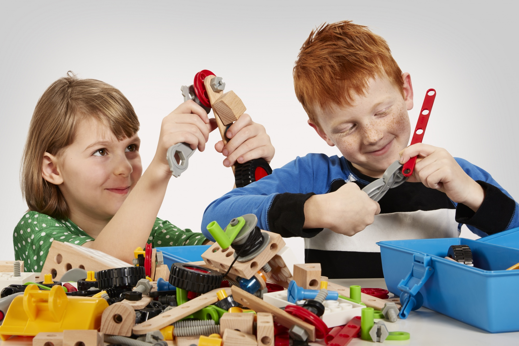 Zwei Kinder bauen mit einem Konstruktionsspielzeug. Der Junge rechts hat rote Haare und trägt ein blaues Hemd.