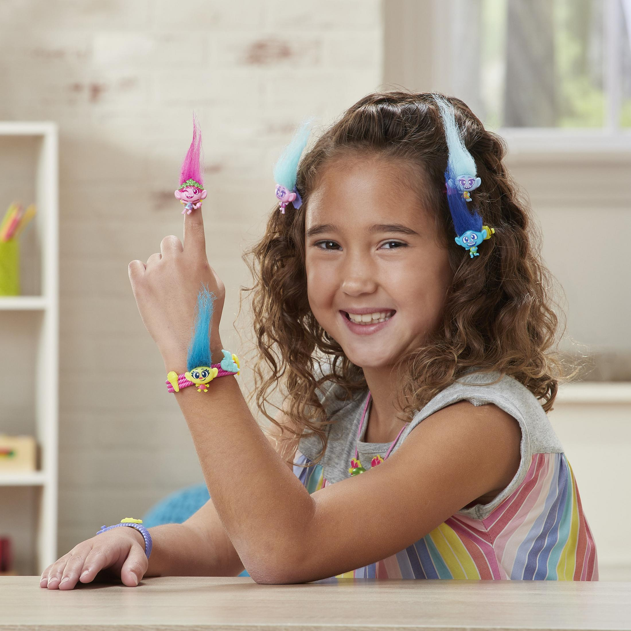 Une fille sourit, portant des figurines de Trolls dans ses cheveux et sur son bras.