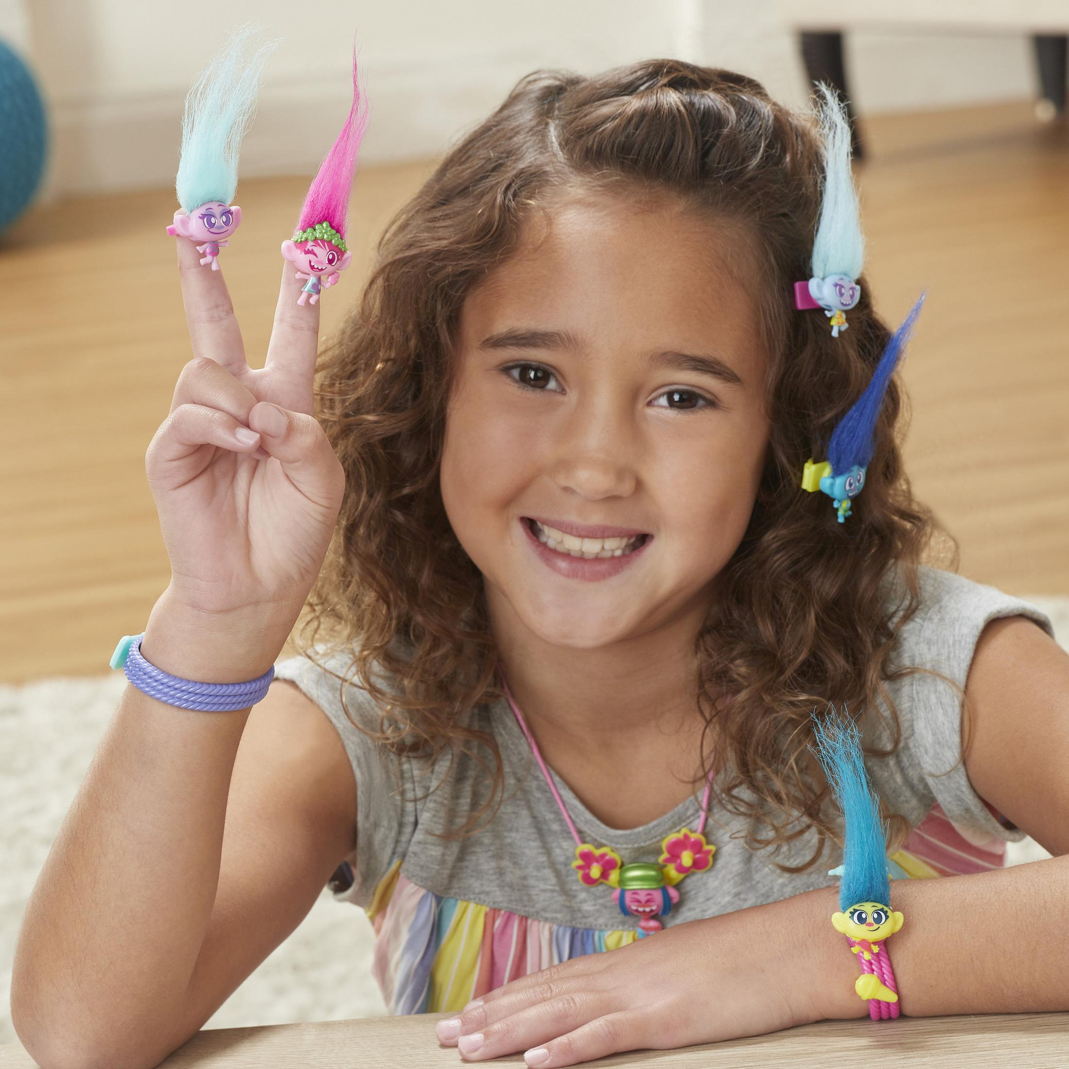 Une fille avec des poupées troll sur les doigts et les cheveux, portant des bijoux.