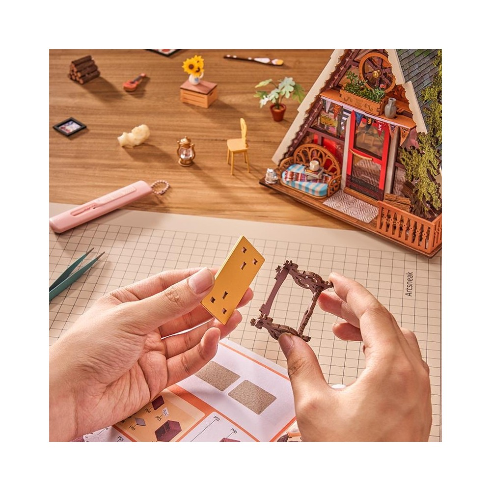 Manos ensamblan un modelo de casa en miniatura con herramientas y piezas pequeñas en mesa.