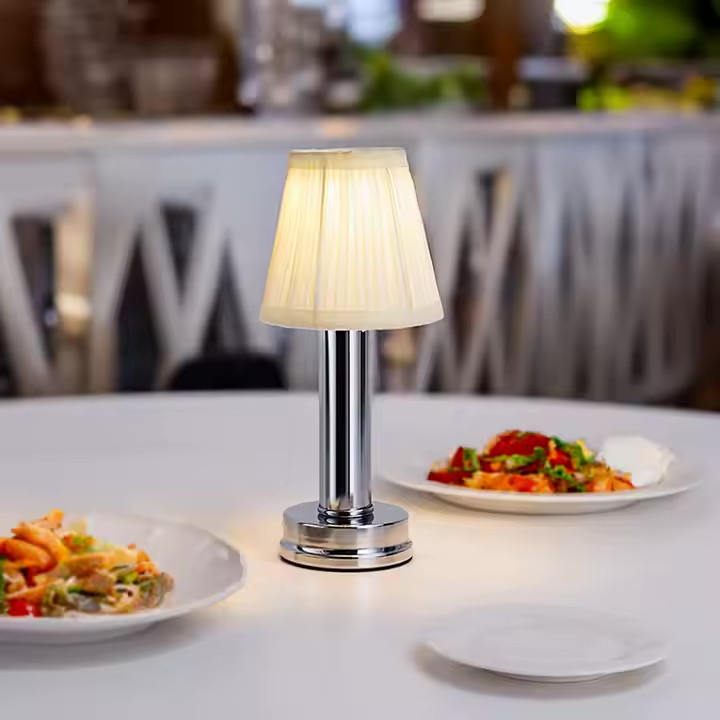 Eine kleine Lampe auf einem Tisch mit Essen, im Hintergrund unscharfe Stühle.