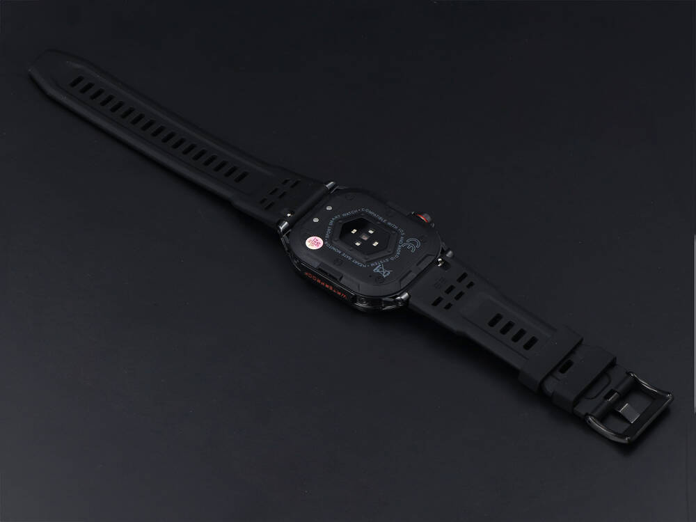 Czarny smartwatch z czarnym paskiem leżący na ciemnym tle.
