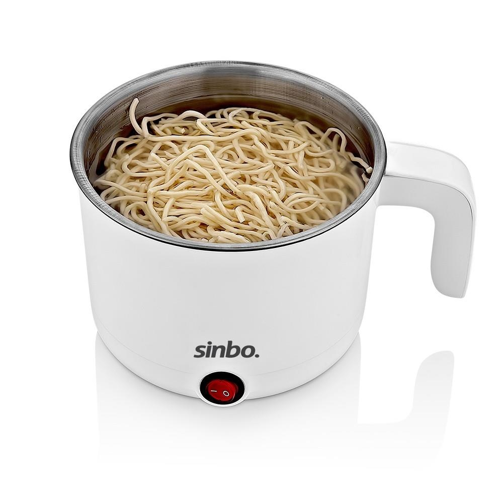 Noodle dolu beyaz bir Sinbo elektrikli tencere ve kırmızı güç düğmesi.
