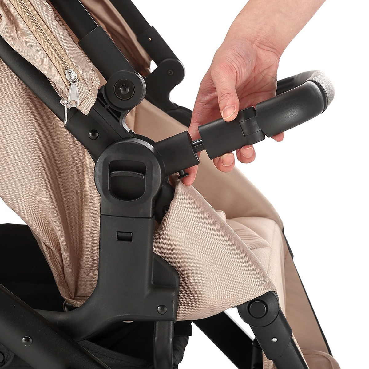Hand befestigt schwarzen Griff an einem beigen Kinderwagengestell mit Reißverschluss.
