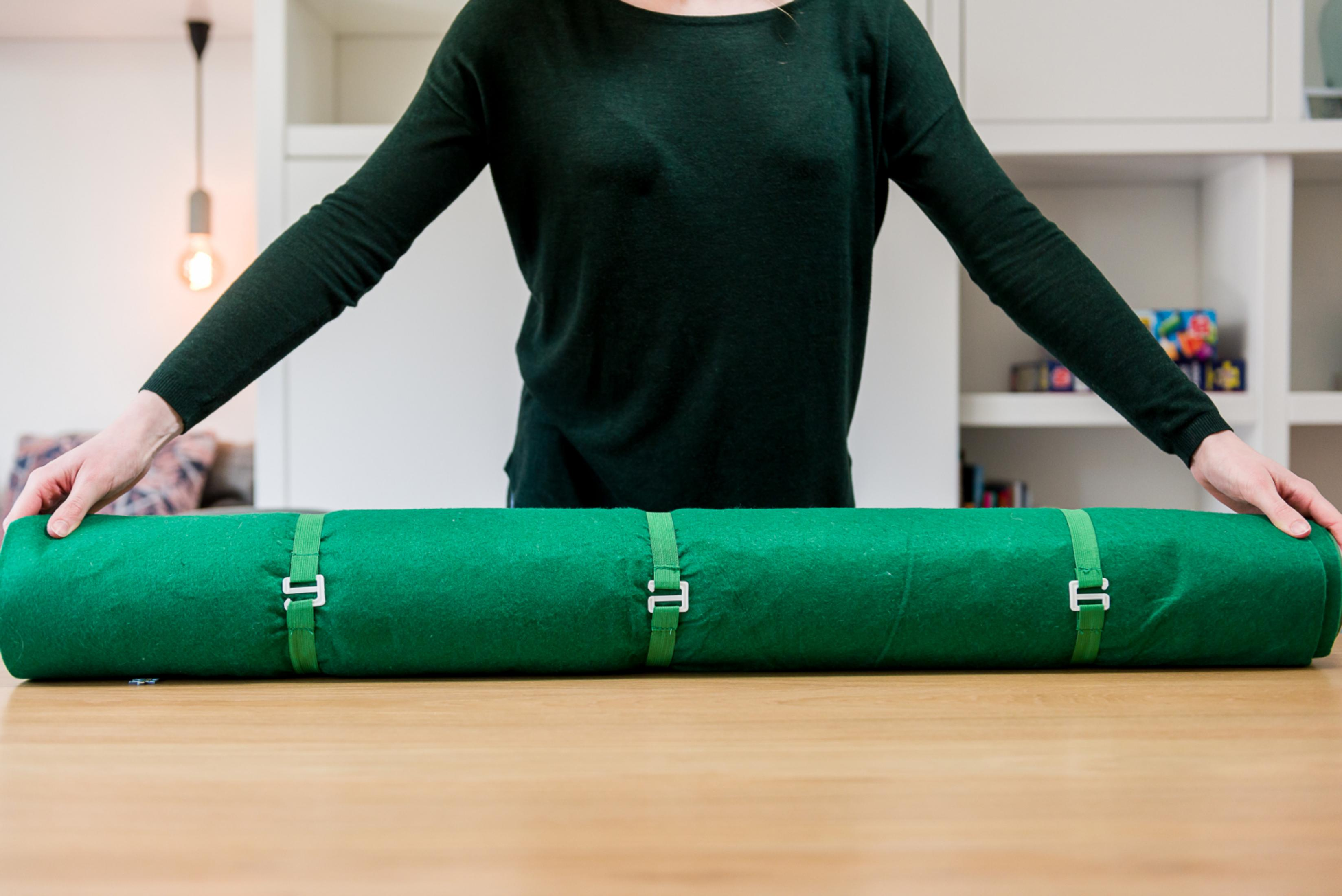 Een persoon rolt een groene mat op met witte gespen op een houten tafel.