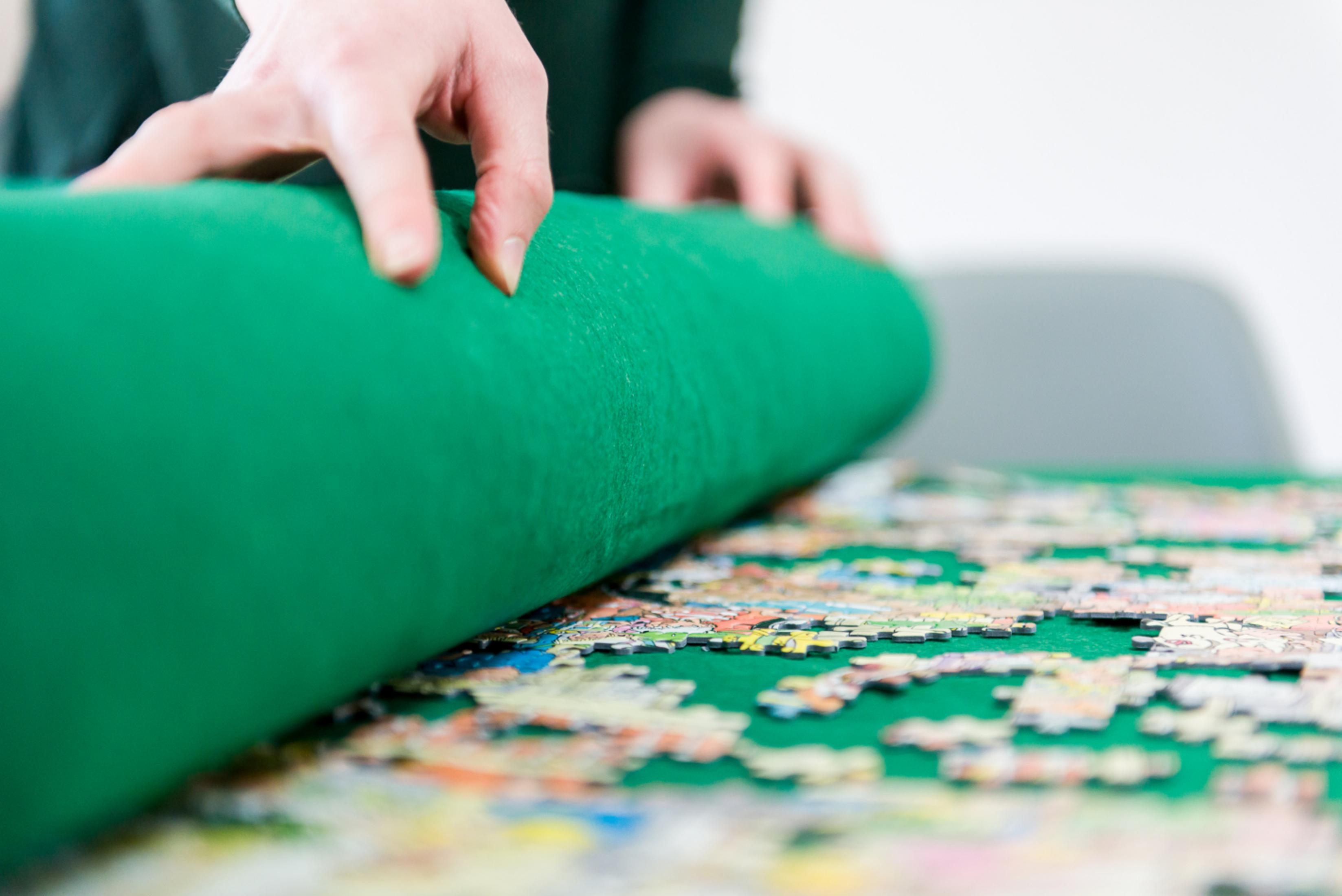 Handen rollen een groene mat over een legpuzzel.