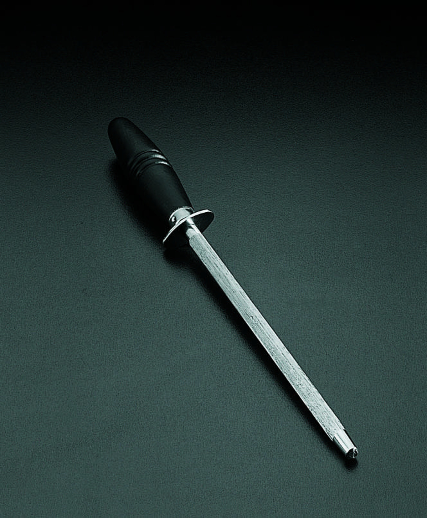 Ein Wetzstahl mit schwarzem Griff und Metallklinge auf dunklem Hintergrund.
