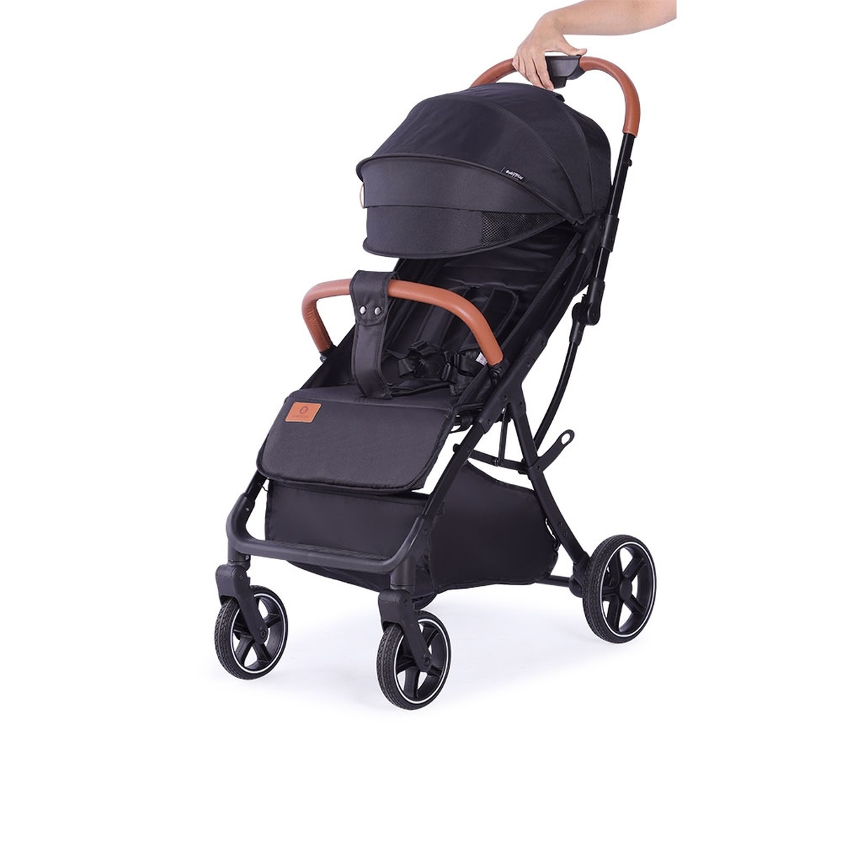 Schwarzer Kinderwagen mit braunen Griffen, der von einer Hand gehalten wird.