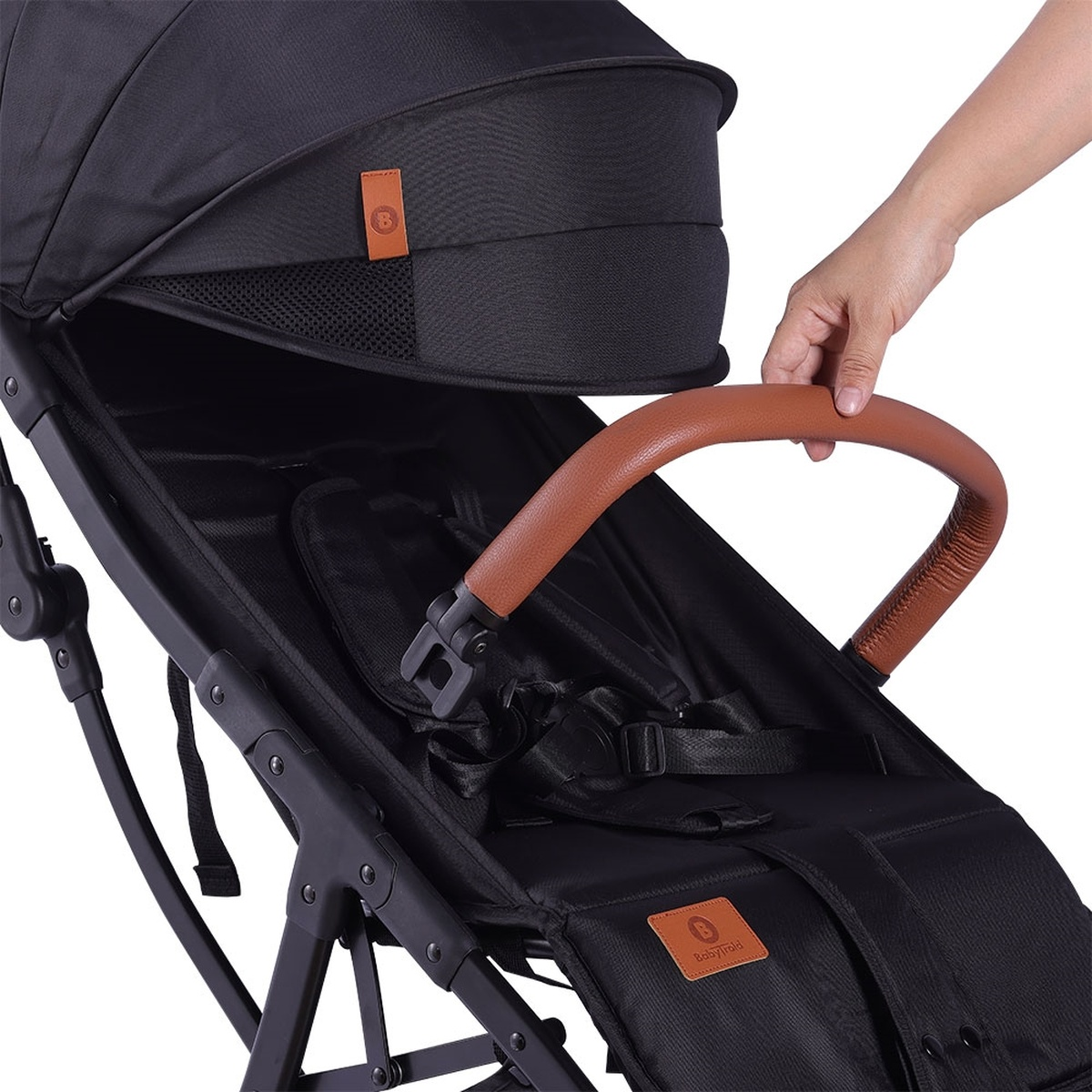 Eine Hand greift nach dem braunen Ledergriff eines schwarzen Kinderwagens.