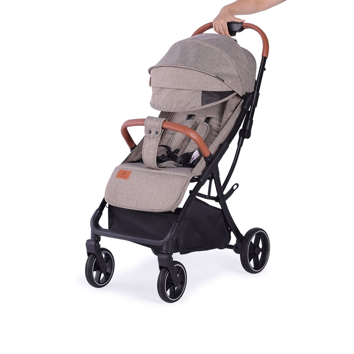 Eine Person schiebt einen beigefarbenen Kinderwagen mit braunen Griffen und schwarzen Rädern.