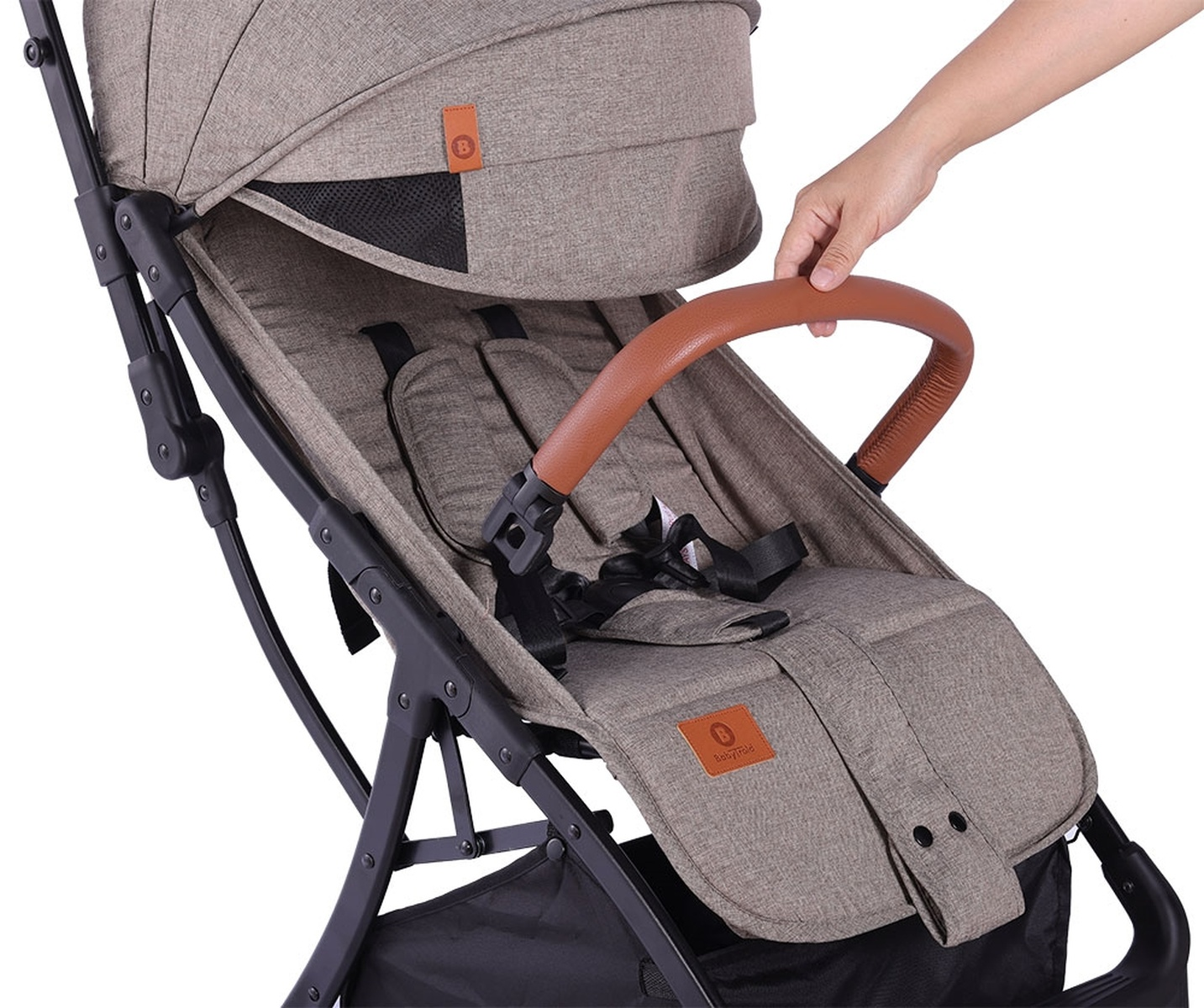 Eine Hand greift nach dem braunen Griff eines Kinderwagens. Verstellbare Gurte sind sichtbar.