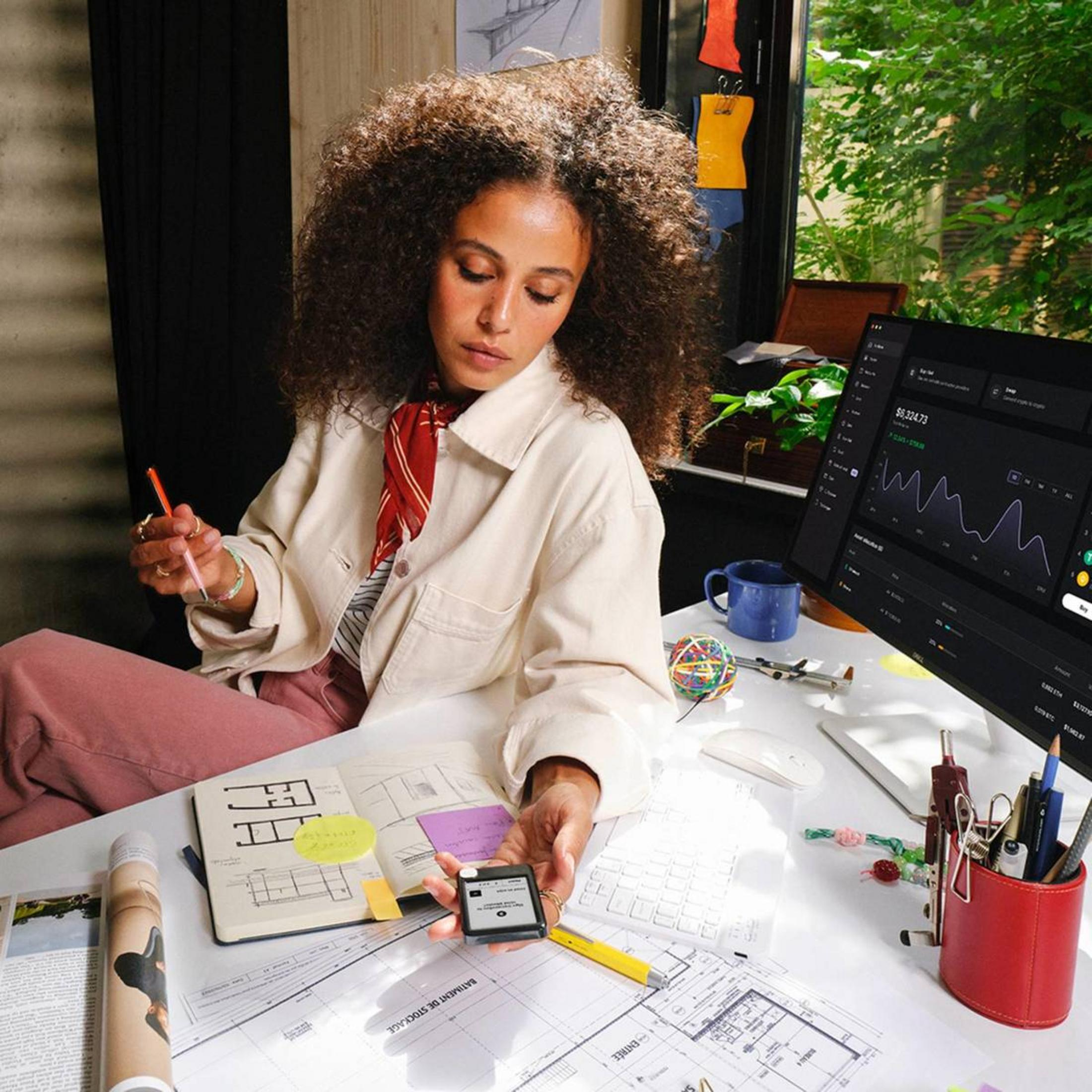 Una mujer se sienta en un escritorio con planos de arquitectura y una computadora.