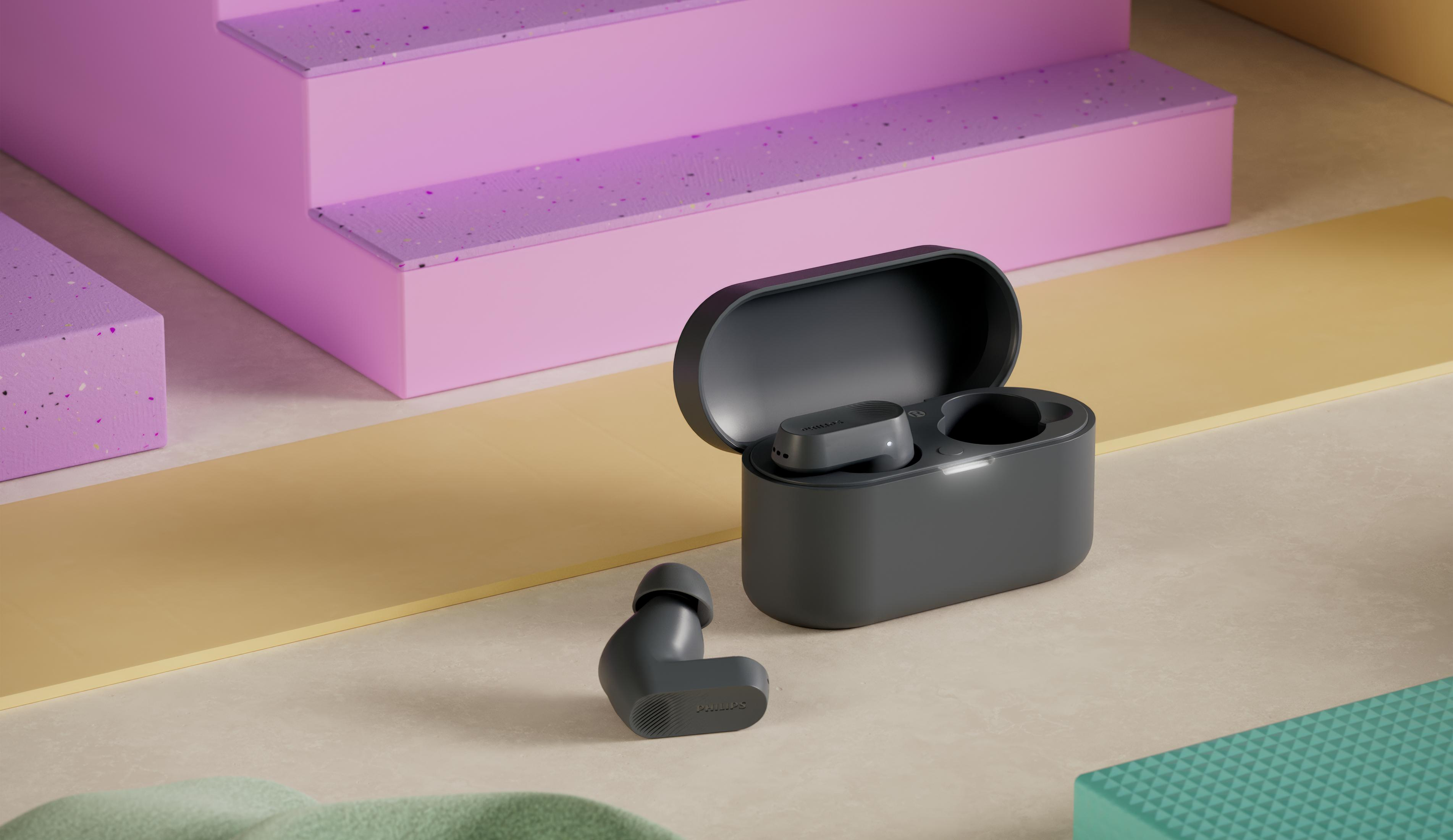 Auriculares inalámbricos gris oscuro con estuche de carga sobre superficie clara.