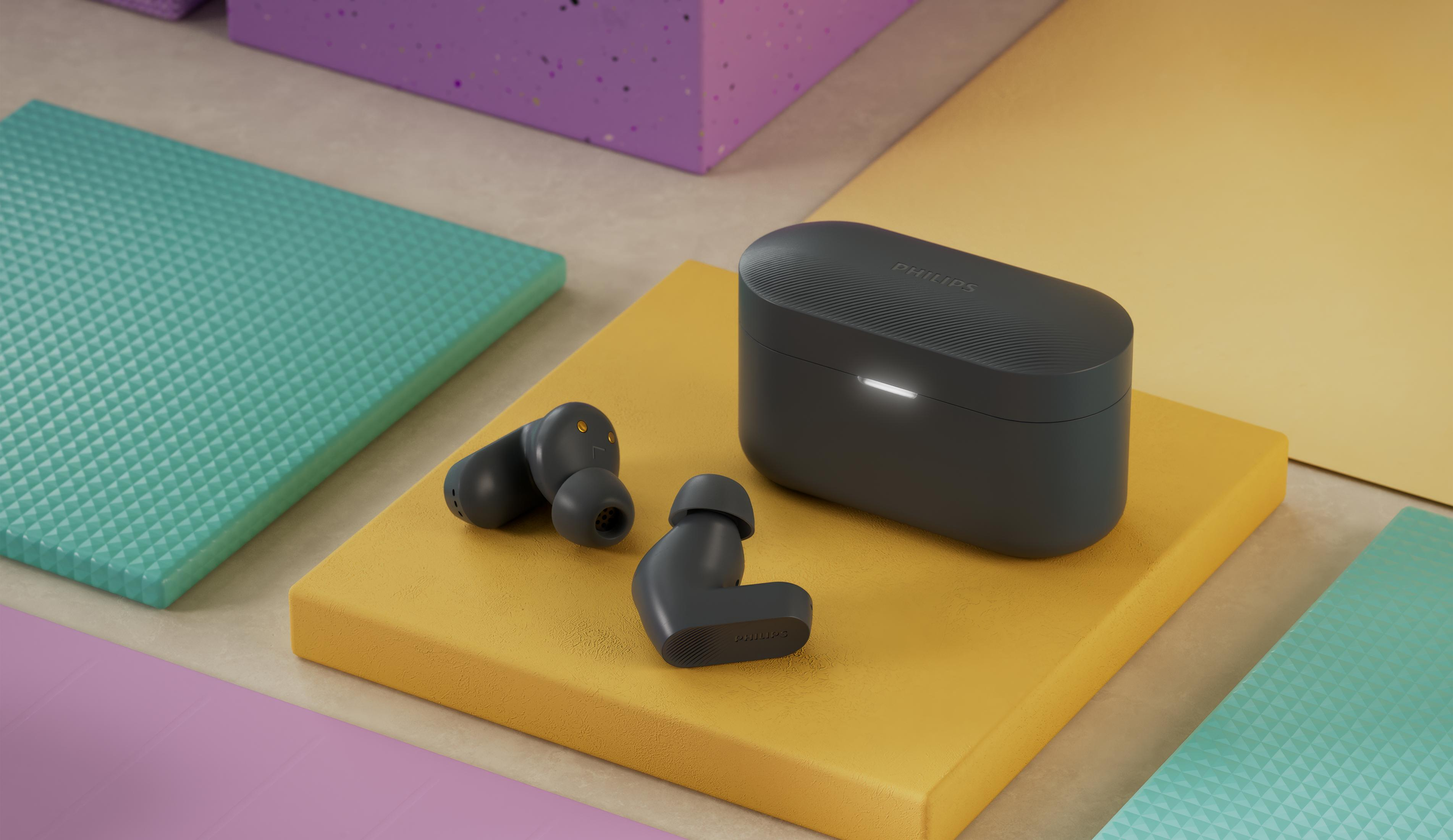 Auriculares inalámbricos gris oscuro con estuche de carga sobre pedestal amarillo.