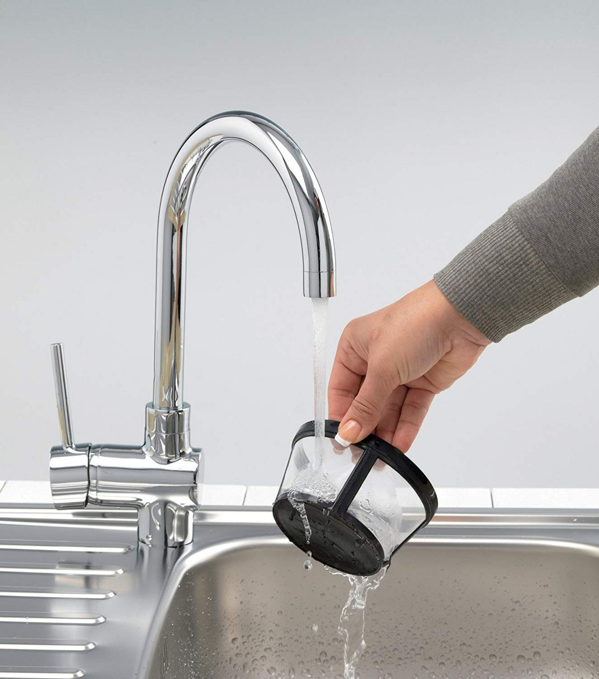 Eine Hand wäscht einen Kaffeefilter unter fließendem Wasser in einer Spüle.