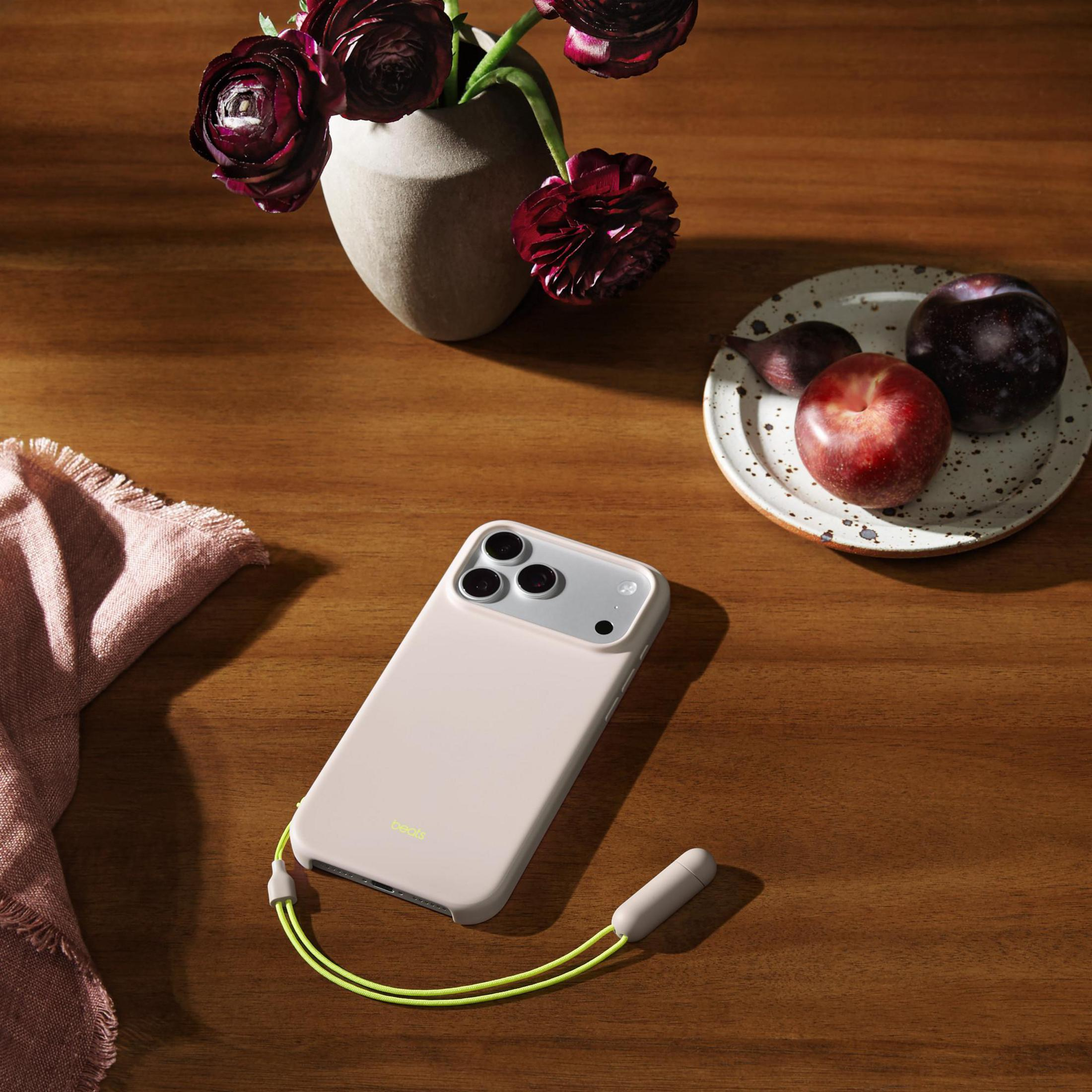 Une coque de téléphone rose pâle avec une lanière jaune fluo sur table en bois.