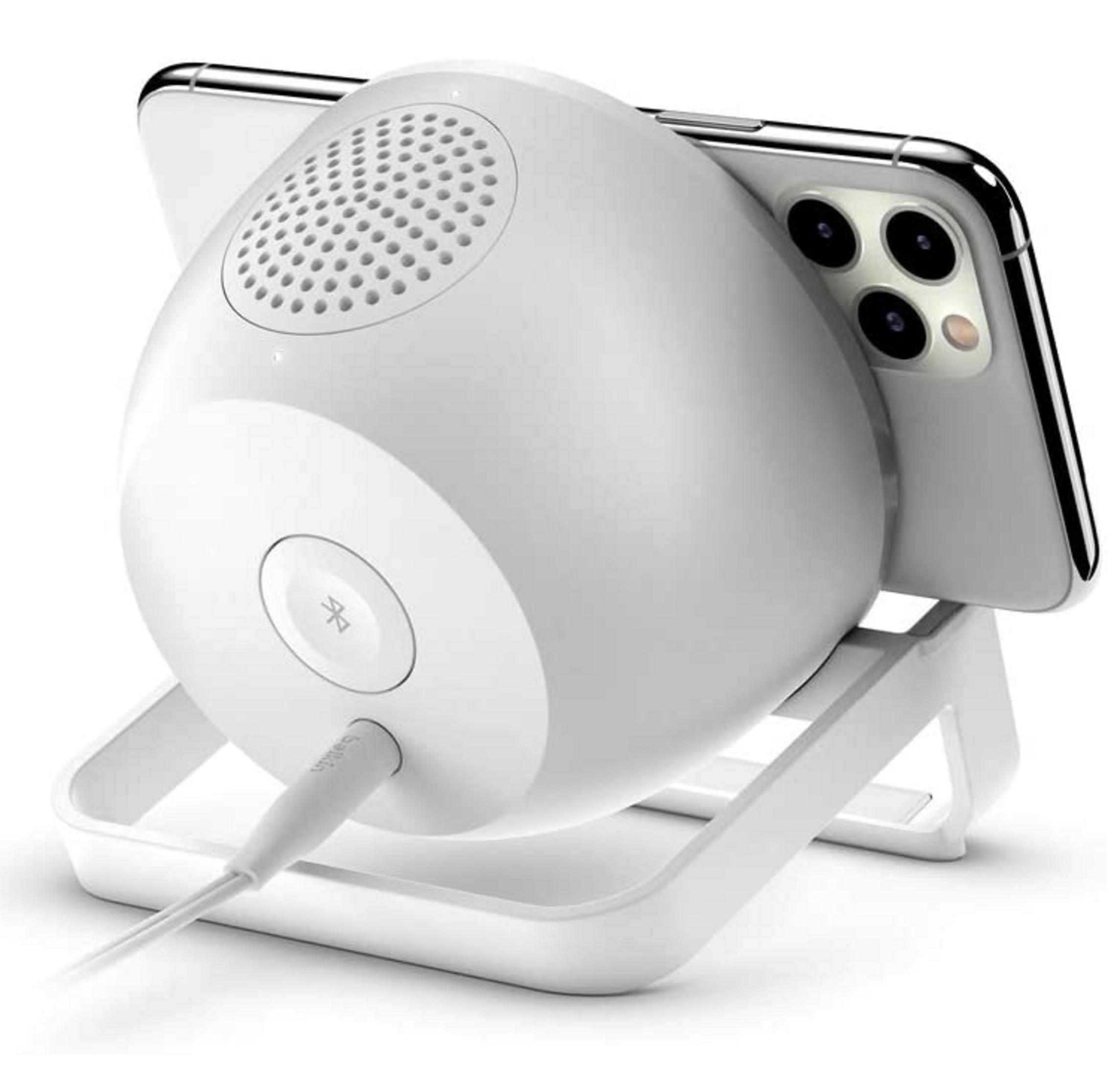 Un altavoz blanco con soporte para teléfono integrado y cable de carga.