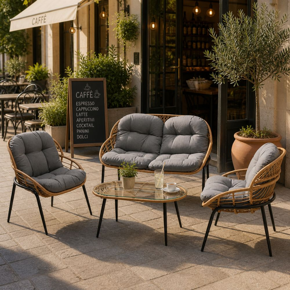 Area salotto esterna con divani in rattan, poltrone, tavolino e piante davanti a un caffè.