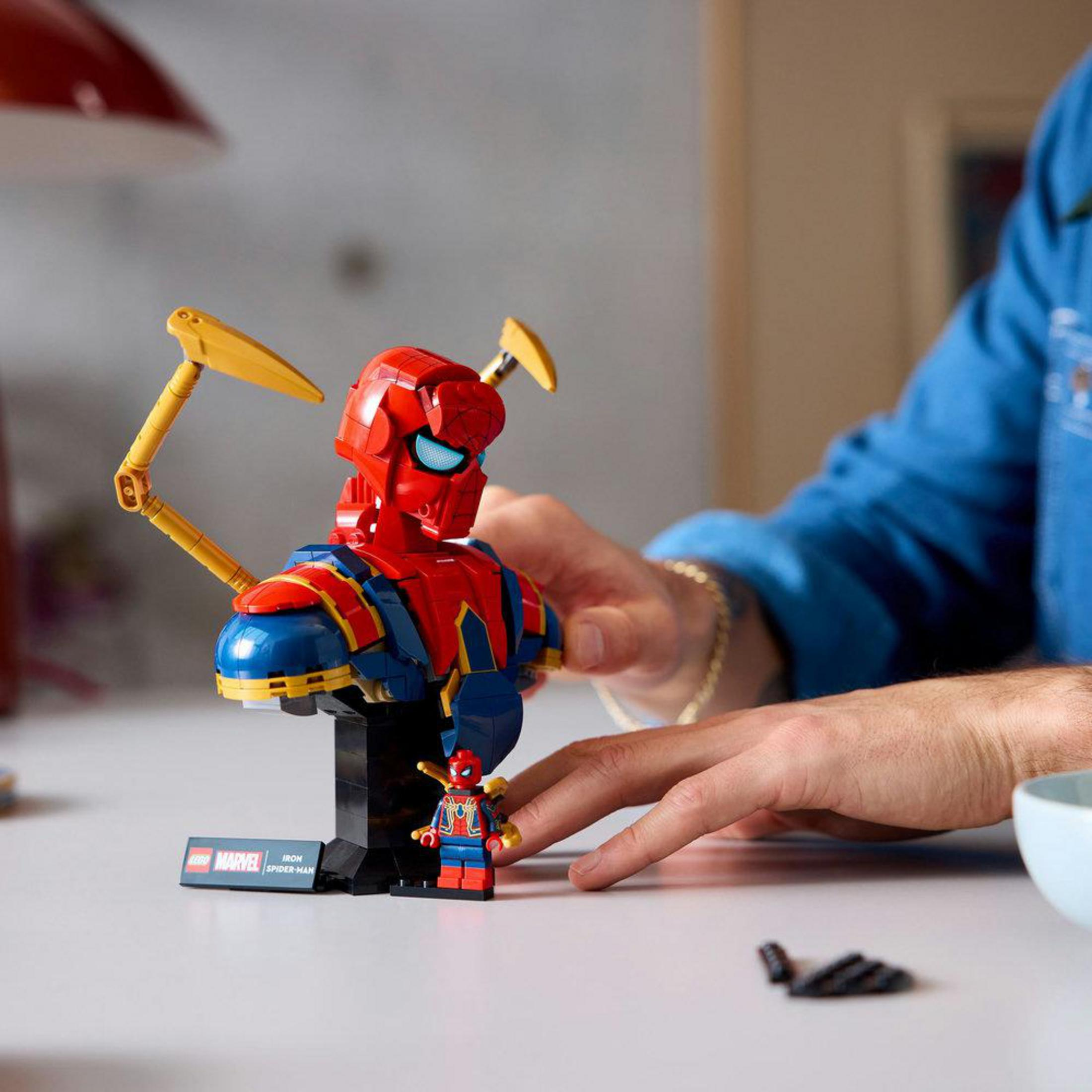 Un hombre construye un Iron Man de Lego rojo y azul con brazos de pinza amarillos.