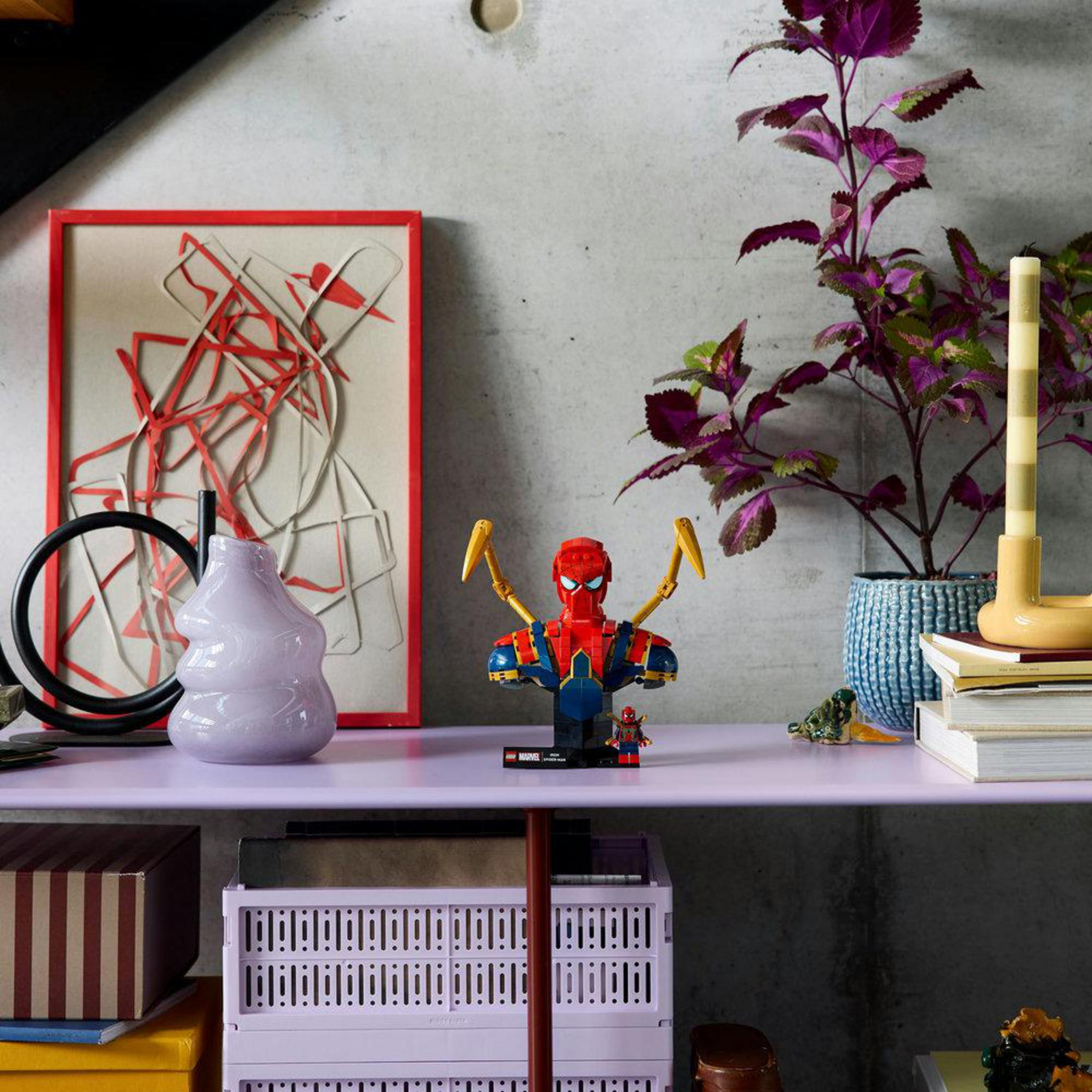 Una construcción de Lego de Spider-Man se sienta en un estante junto a un jarrón y una planta.