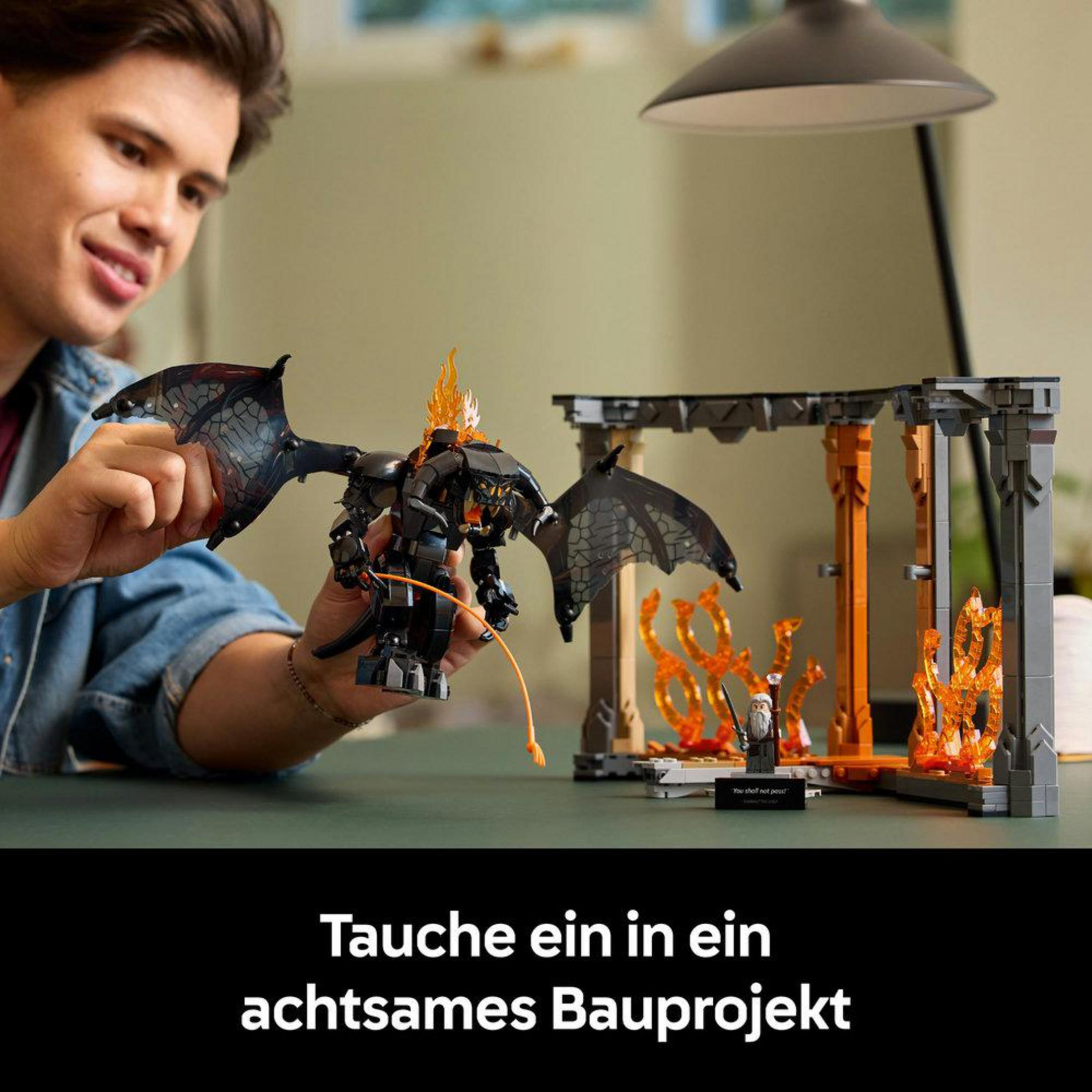 Mężczyzna buduje zestaw LEGO z smokiem i mostem z płomieniami.