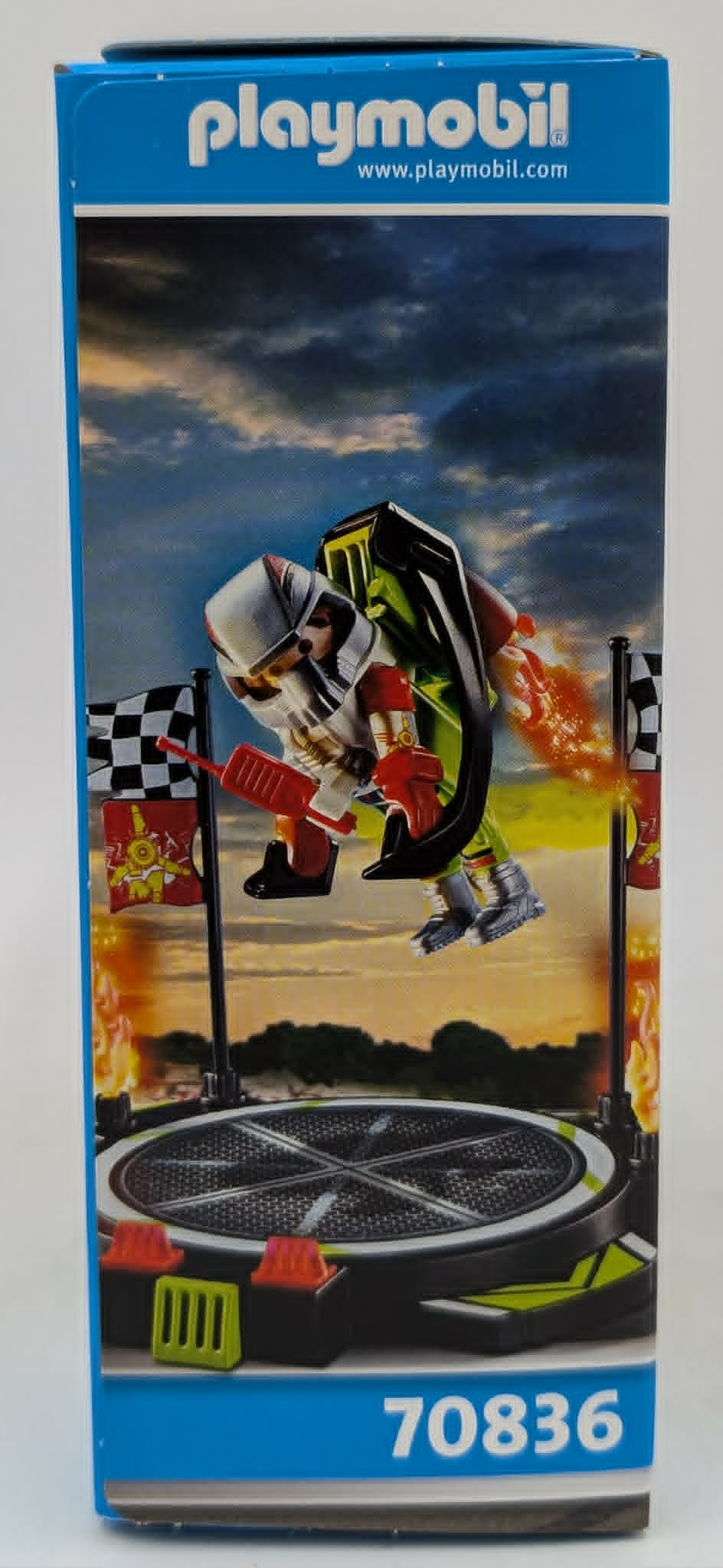 Playmobil-Figur in Raketenrucksack auf Startplattform mit Fahnen und Flammen.
