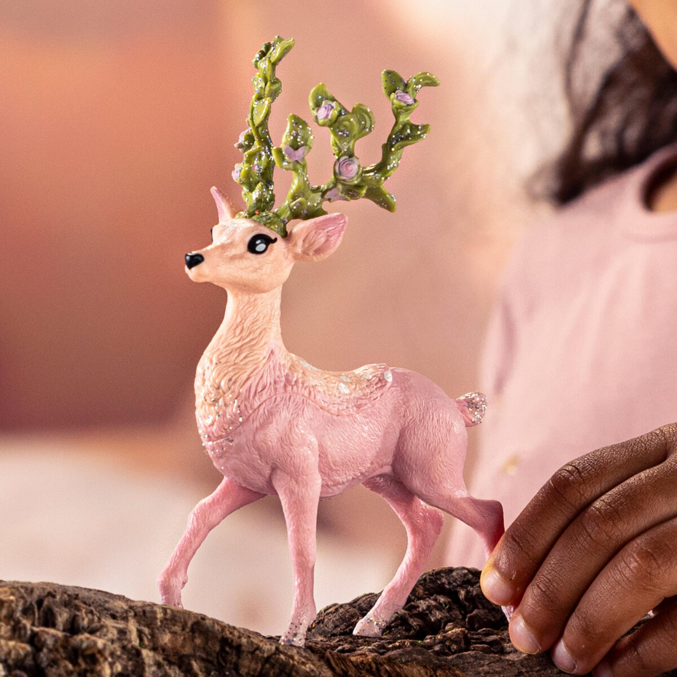 Una figurina di cervo rosa con corna verdi e fiori sta su un tronco.