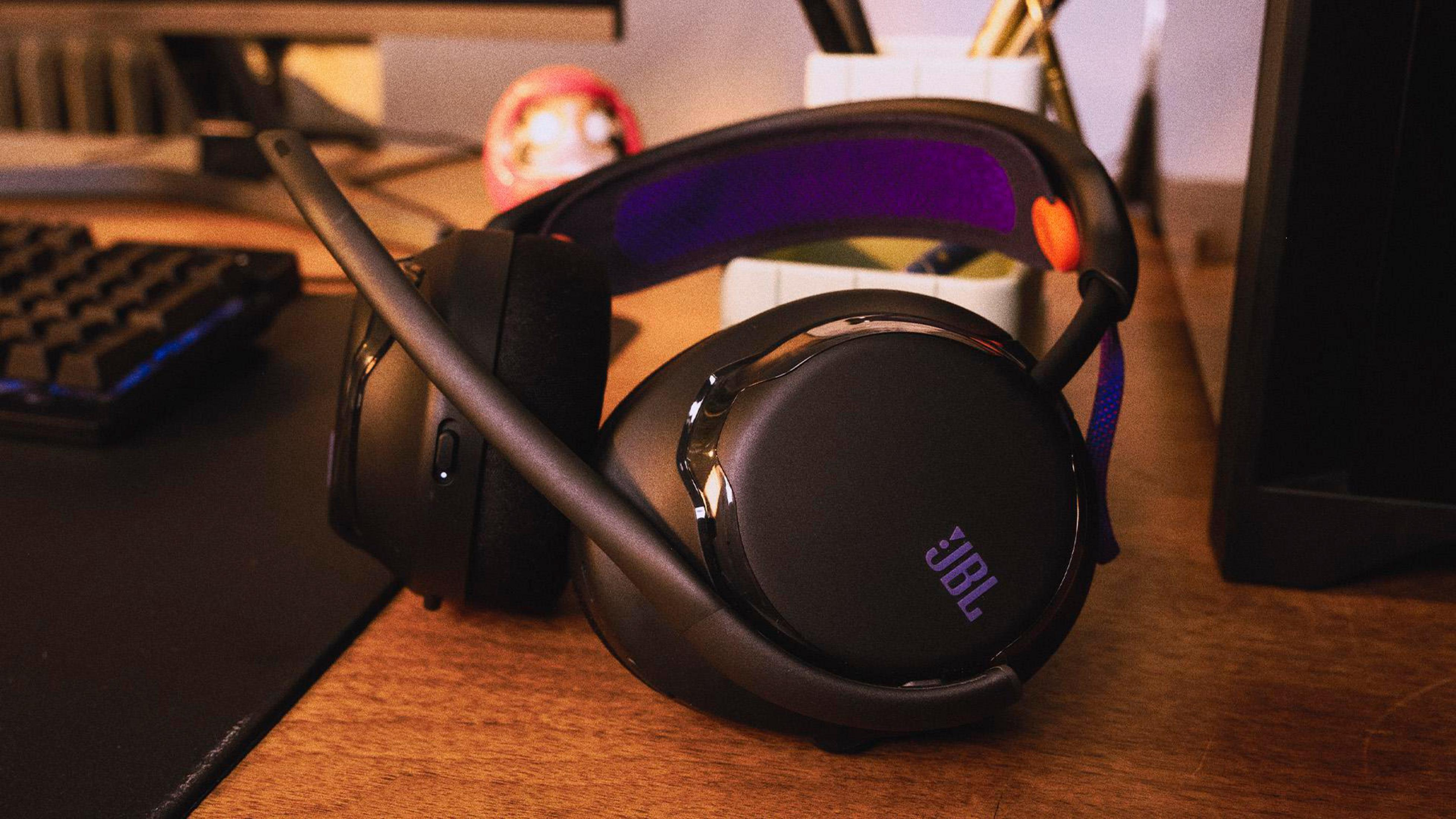 Cuffie JBL nere con accenti viola su una scrivania di legno.