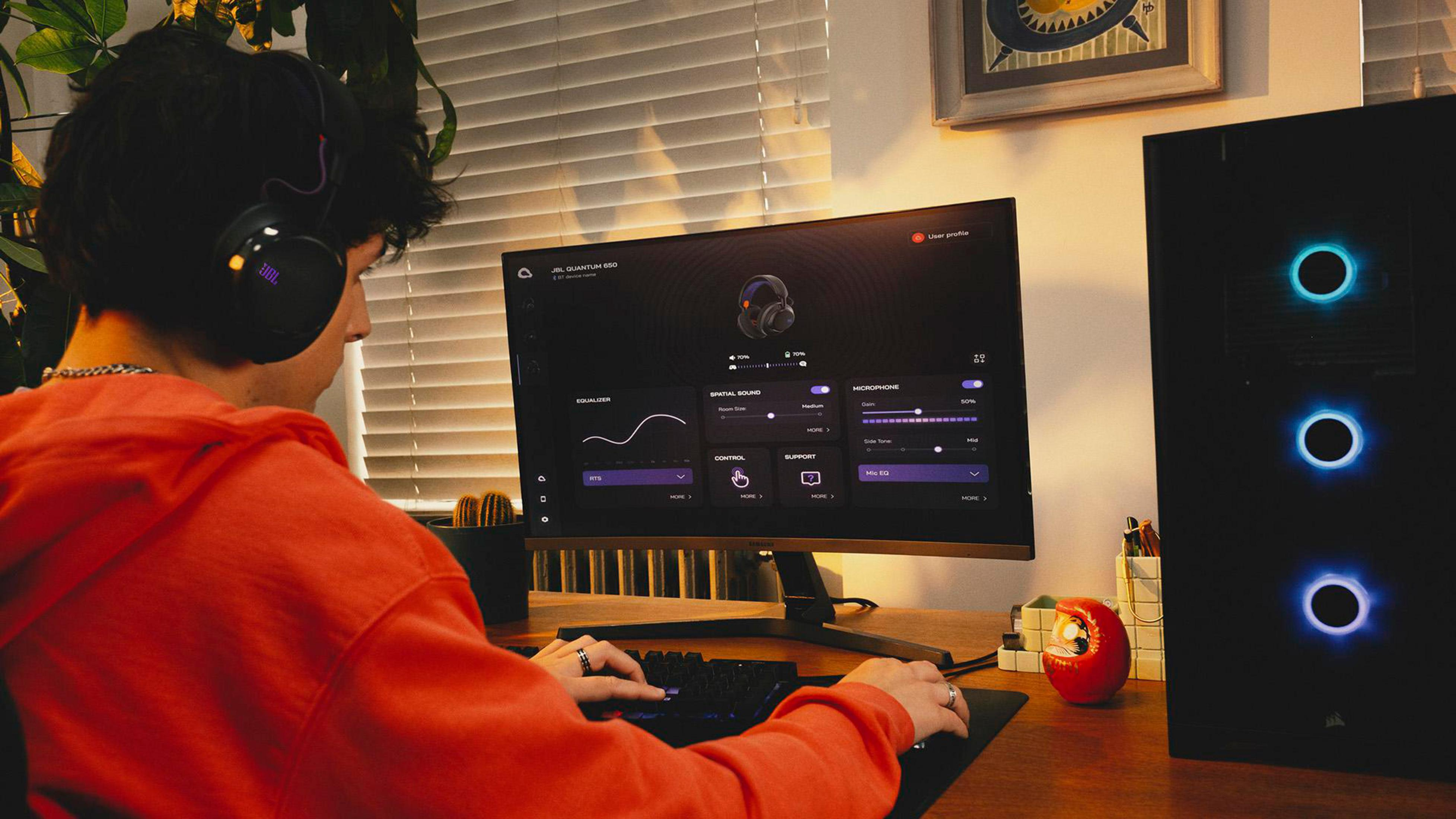 Uomo con cuffie gioca al PC. Il monitor mostra il software JBL Quantum 650.