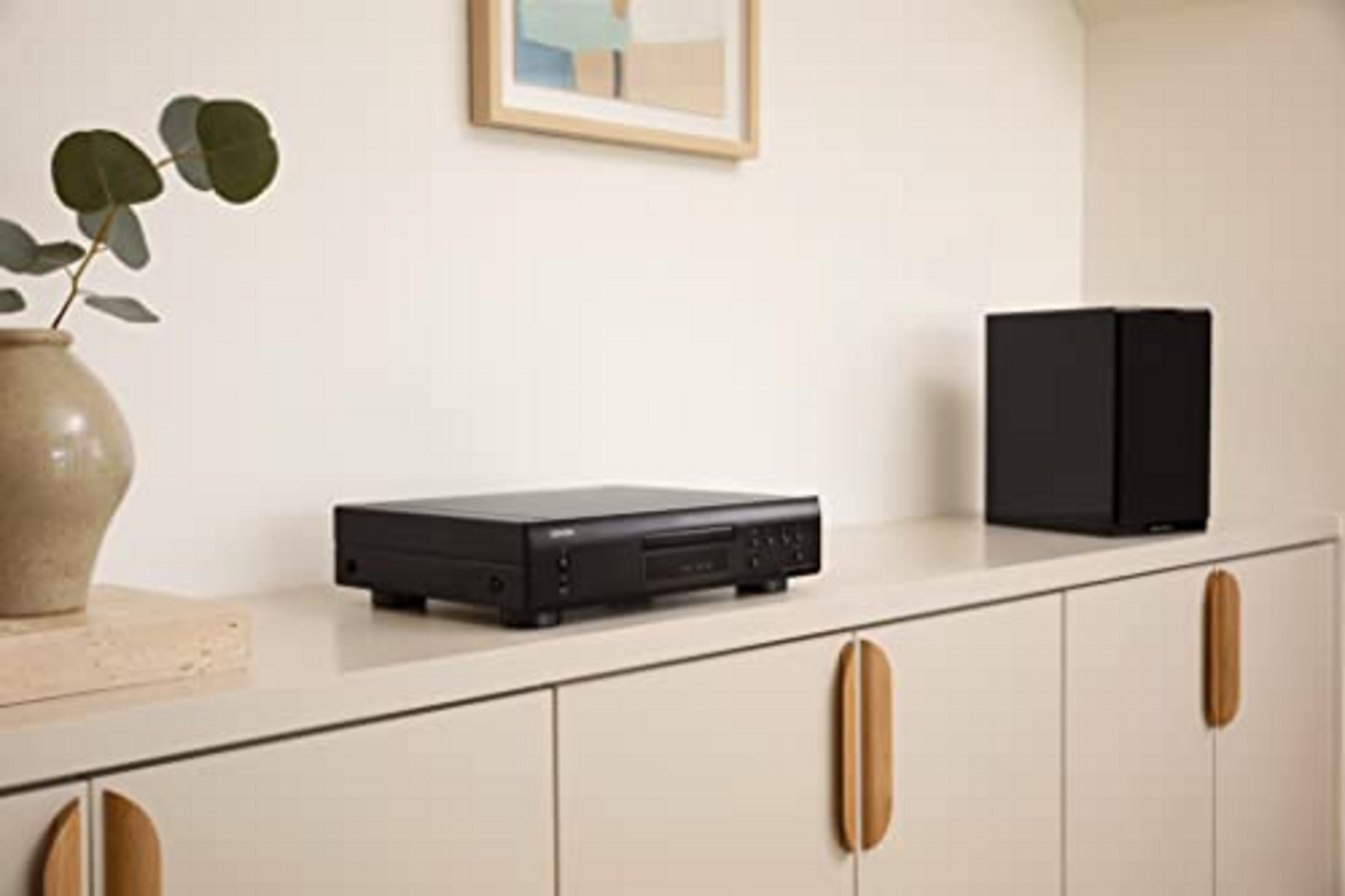 Un reproductor de CD negro y un altavoz negro sobre un mueble blanco.
