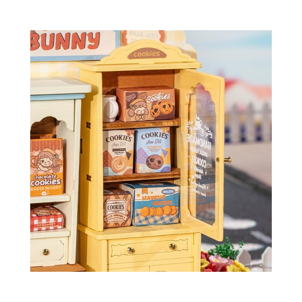 Çikolata kutuları ve beyaz bir kupanın sergilendiği raflı sarı dolap. "BUNNY" ve "cookies" yazısı görünür.