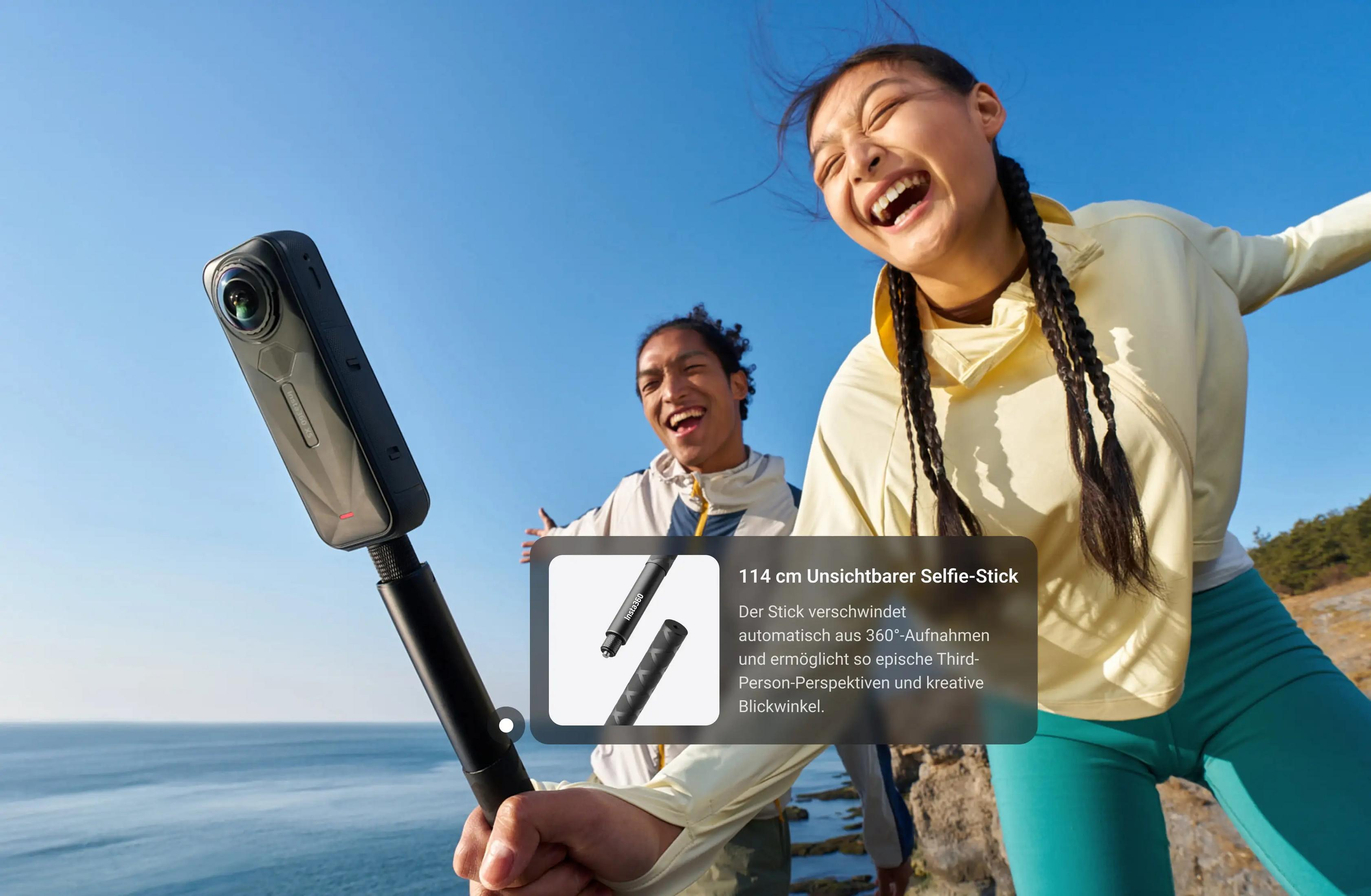 Zwei lachende Personen im Freien, eine hält eine 360-Grad-Kamera auf einem Selfie-Stick.
