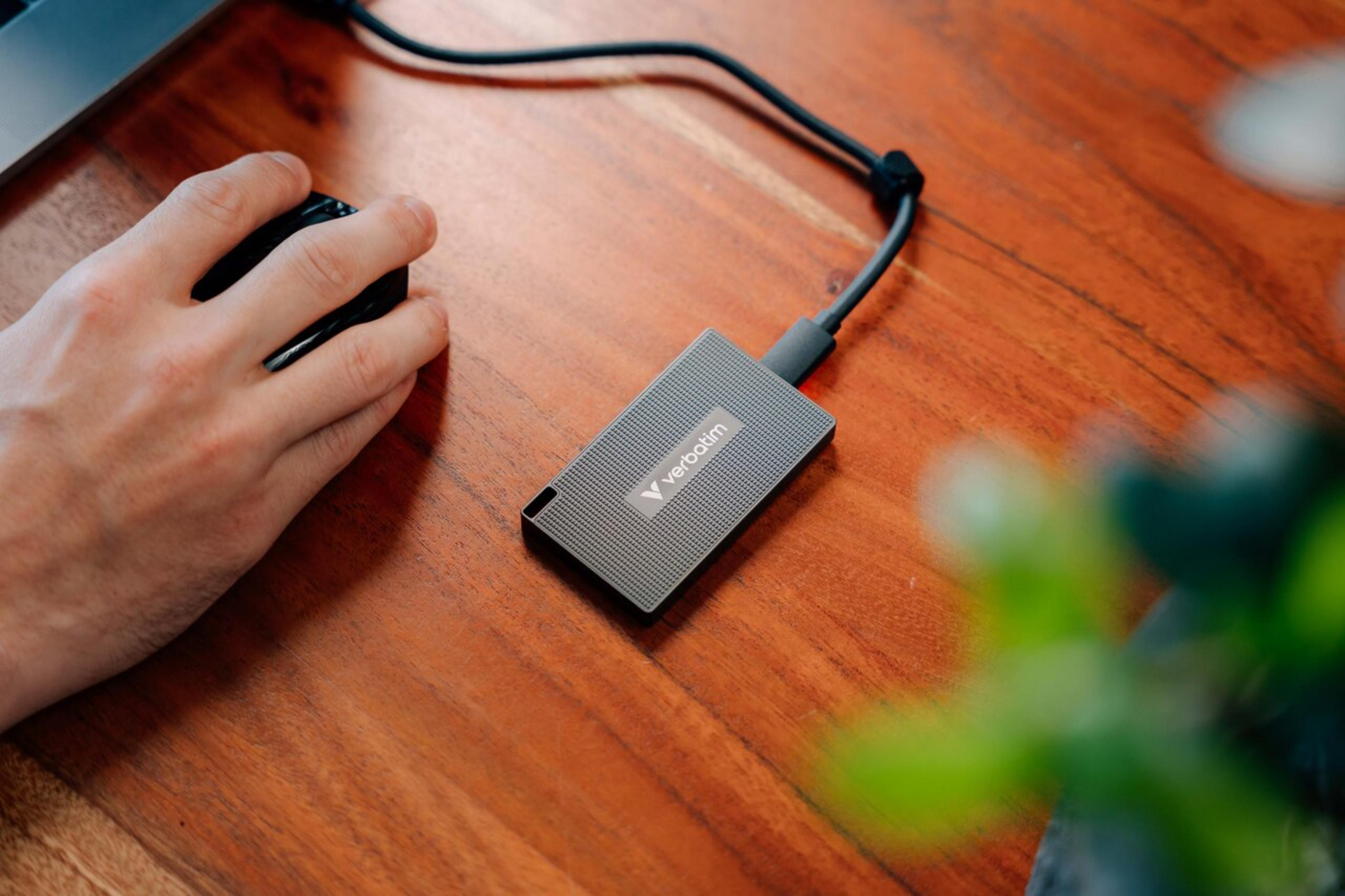 Una mano usa un mouse nero accanto a un'unità esterna grigia su una scrivania di legno.