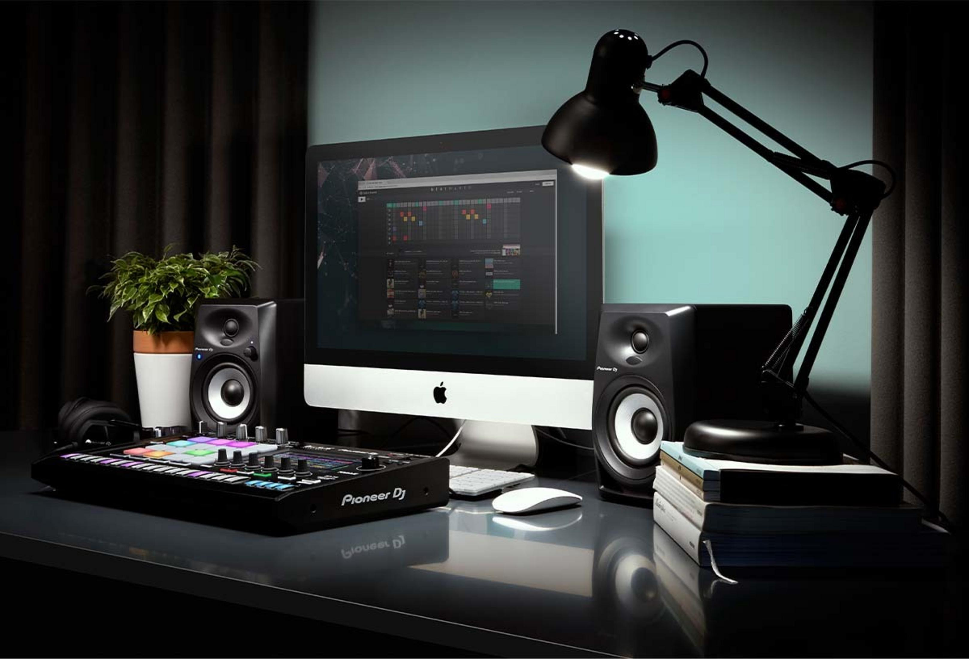 Una postazione da scrivania con un iMac, controller Pioneer DJ, altoparlanti, cuffie e una pianta.