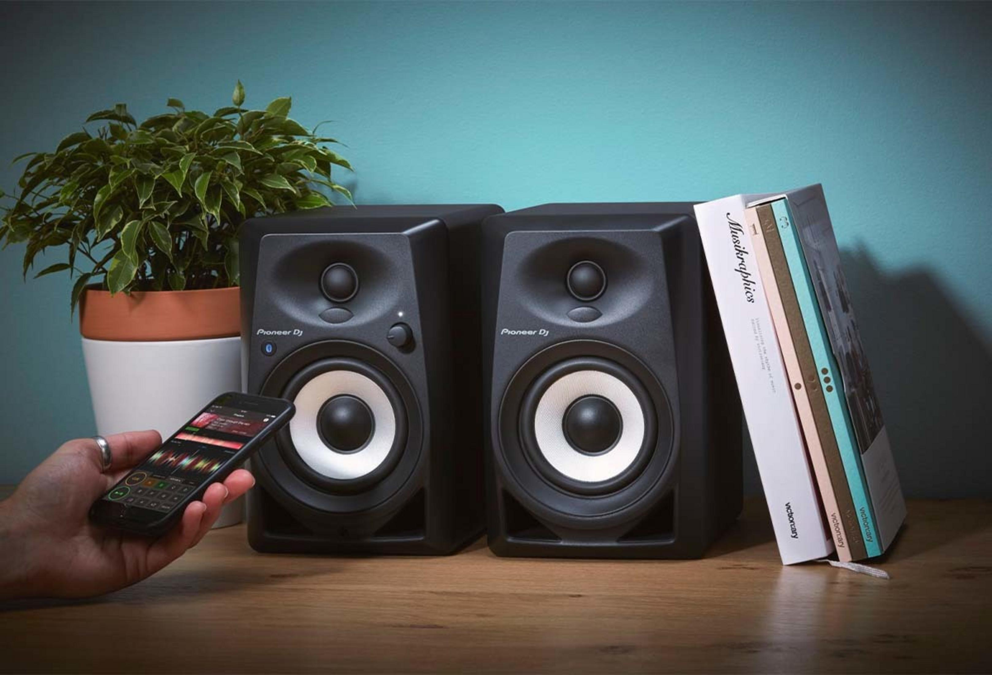 Due altoparlanti Pioneer DJ neri su tavolo in legno con smartphone.
