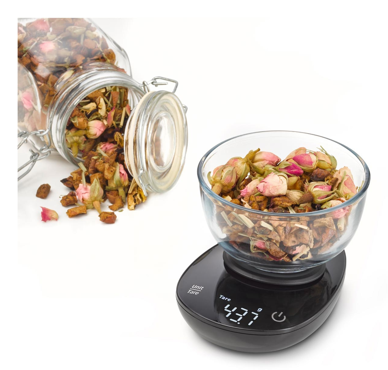 Boutons de rose séchés et herbes dans un bol en verre sur une balance de cuisine.