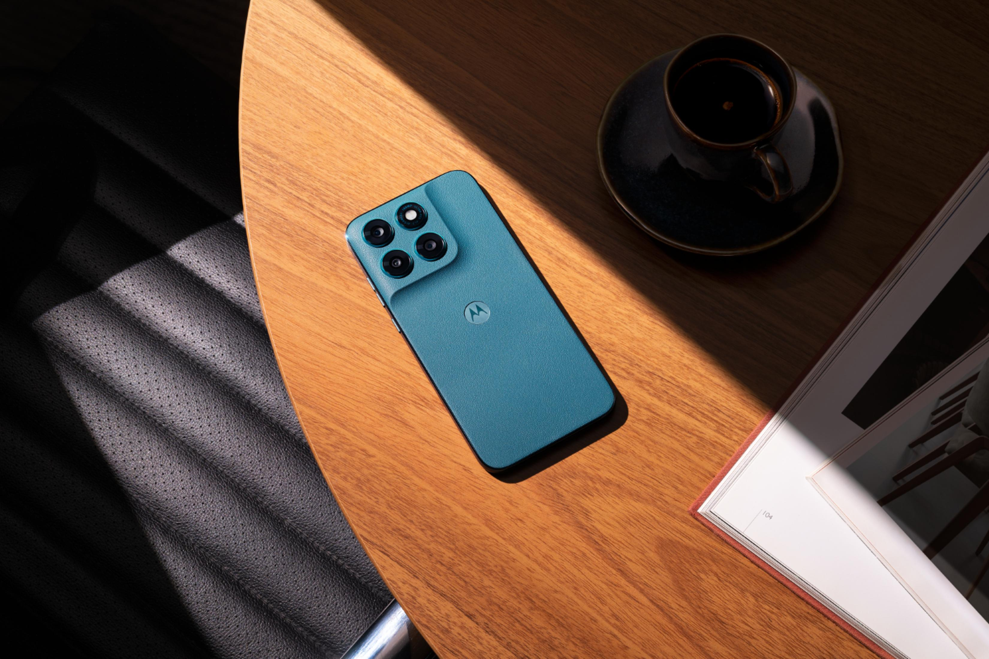 Un telefono Motorola blu è appoggiato su un tavolo di legno accanto a una tazzina di caffè.