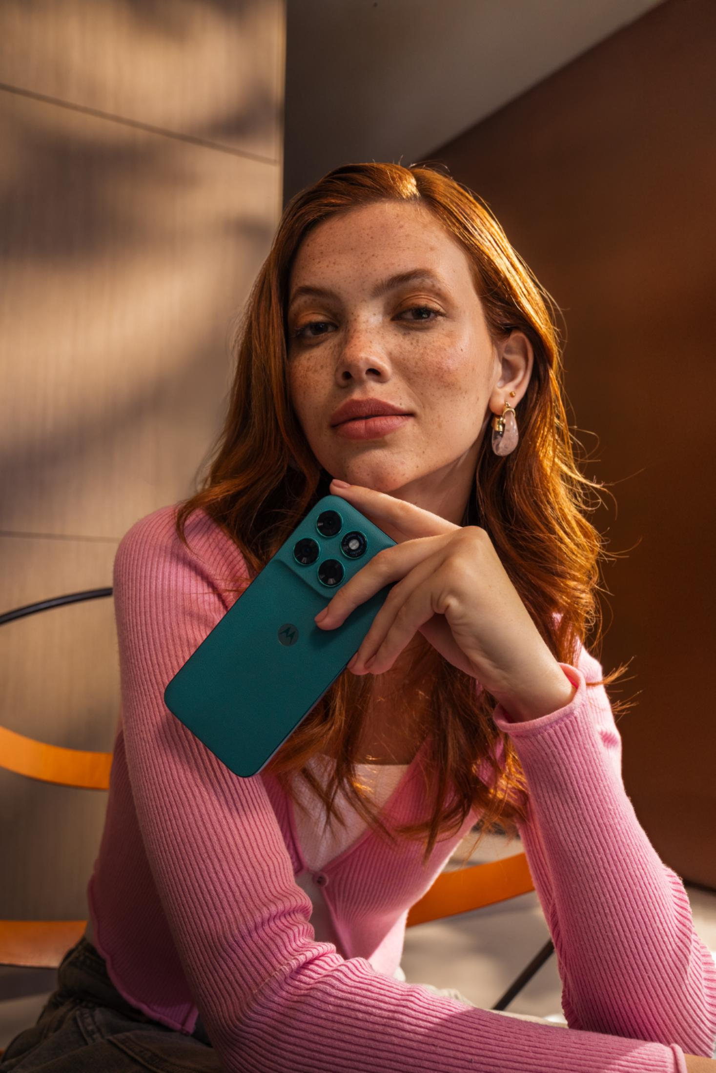 Donna dai capelli rossi tiene un telefono verde acqua, indossa un cardigan rosa.