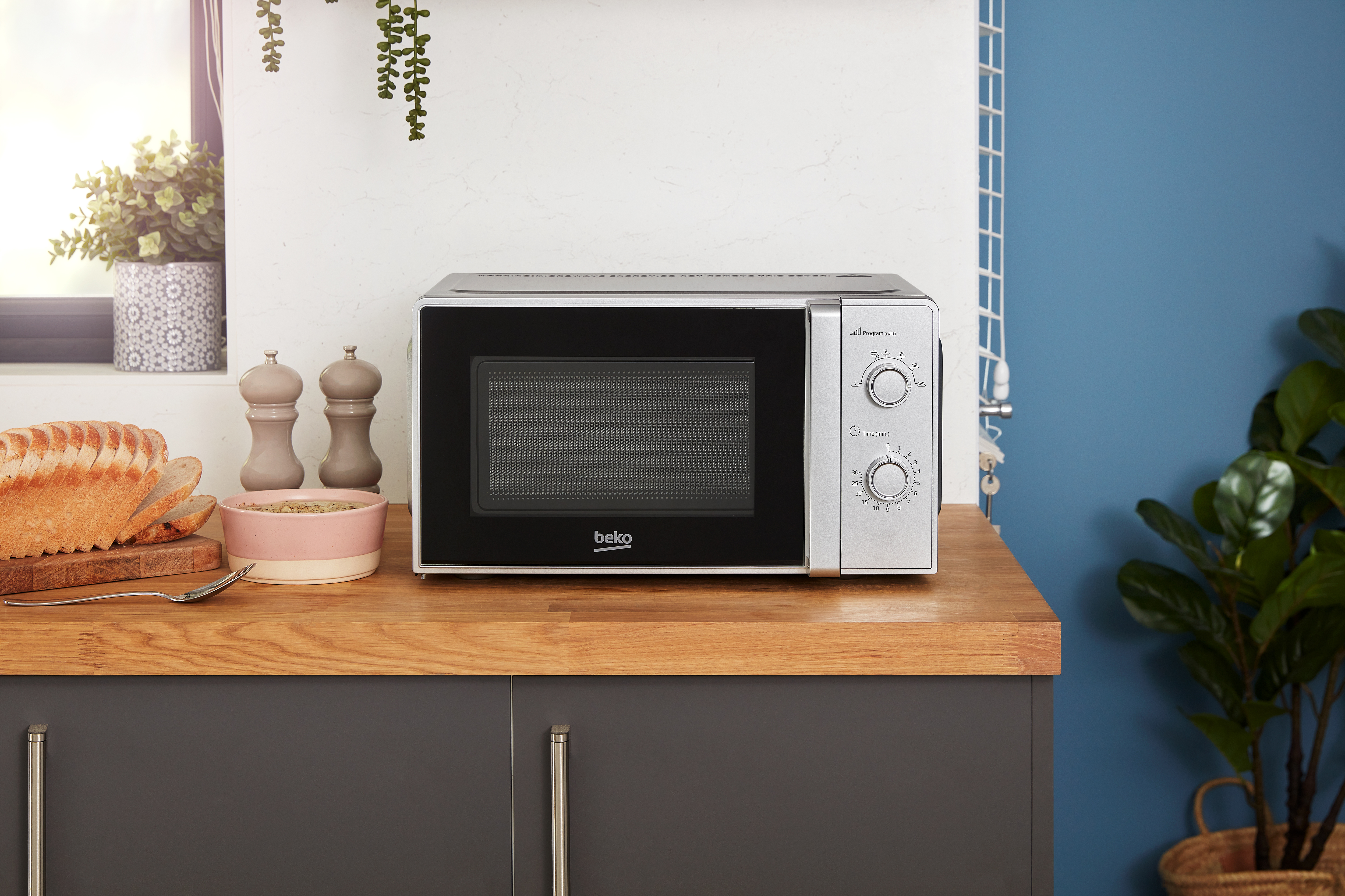 Een Beko magnetron staat op een houten aanrecht naast brood en een kom.
