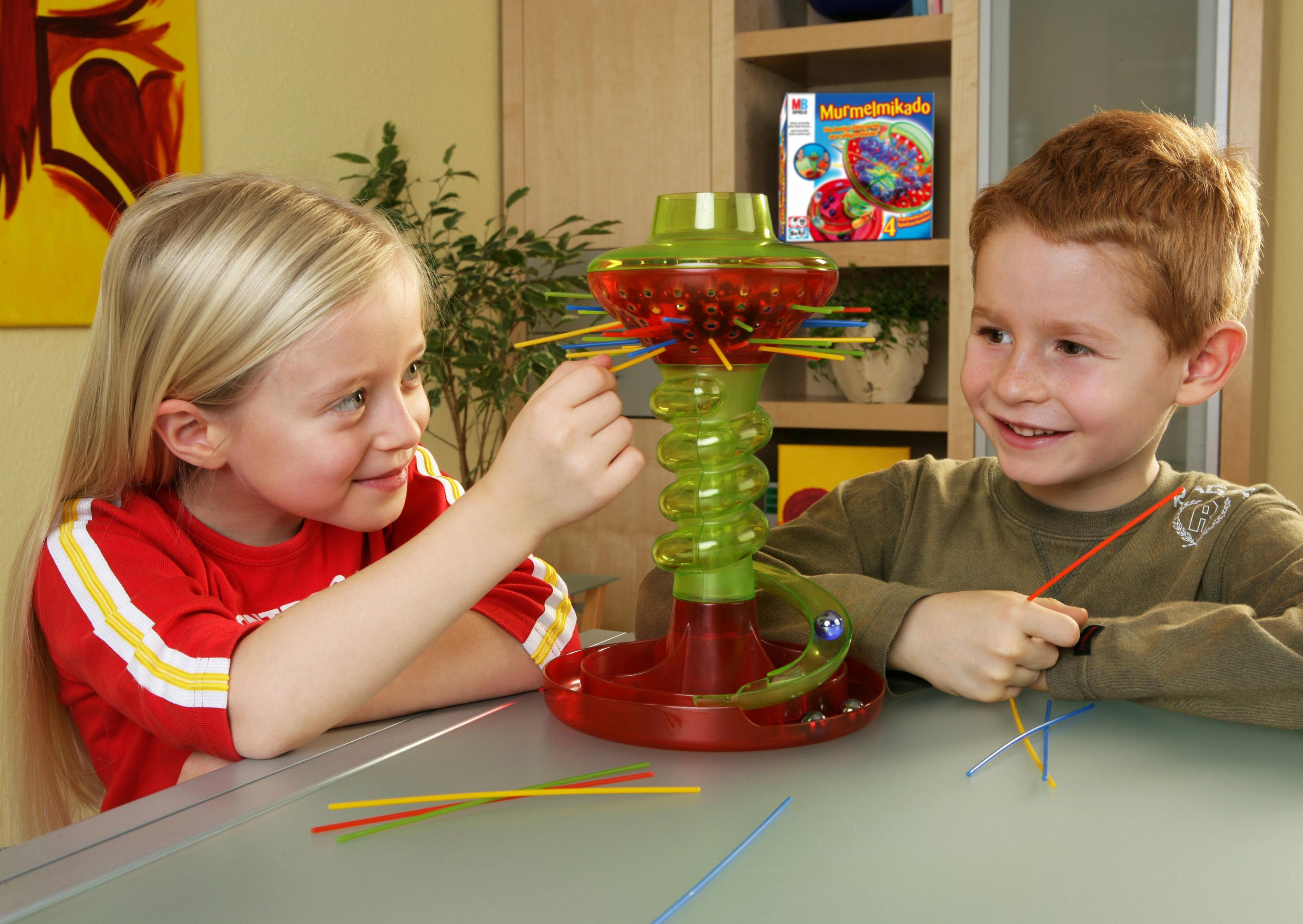 Zwei Kinder spielen Murmelmikado mit bunten Stäbchen und Murmeln auf einem Tisch.