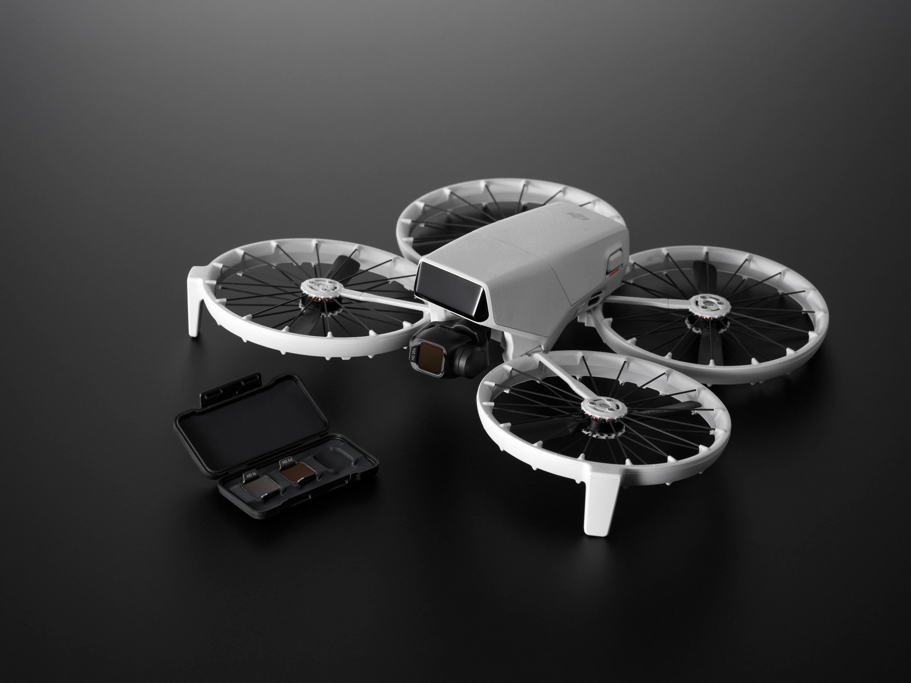 Un modello di drone grigio con quattro eliche e una telecamera. Accanto si trova una scatola nera aperta.