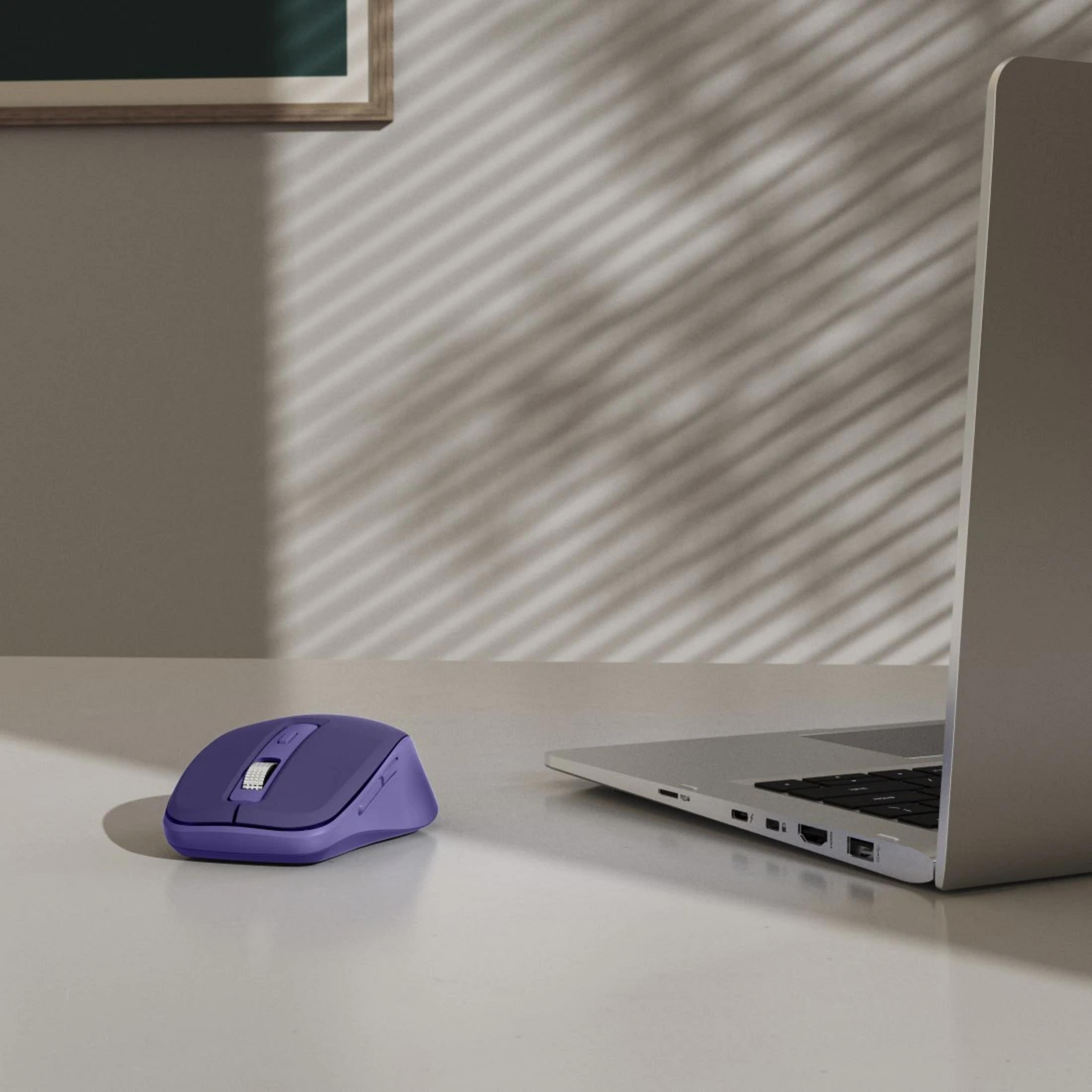 Un mouse viola è accanto a un laptop d'argento su un tavolo.