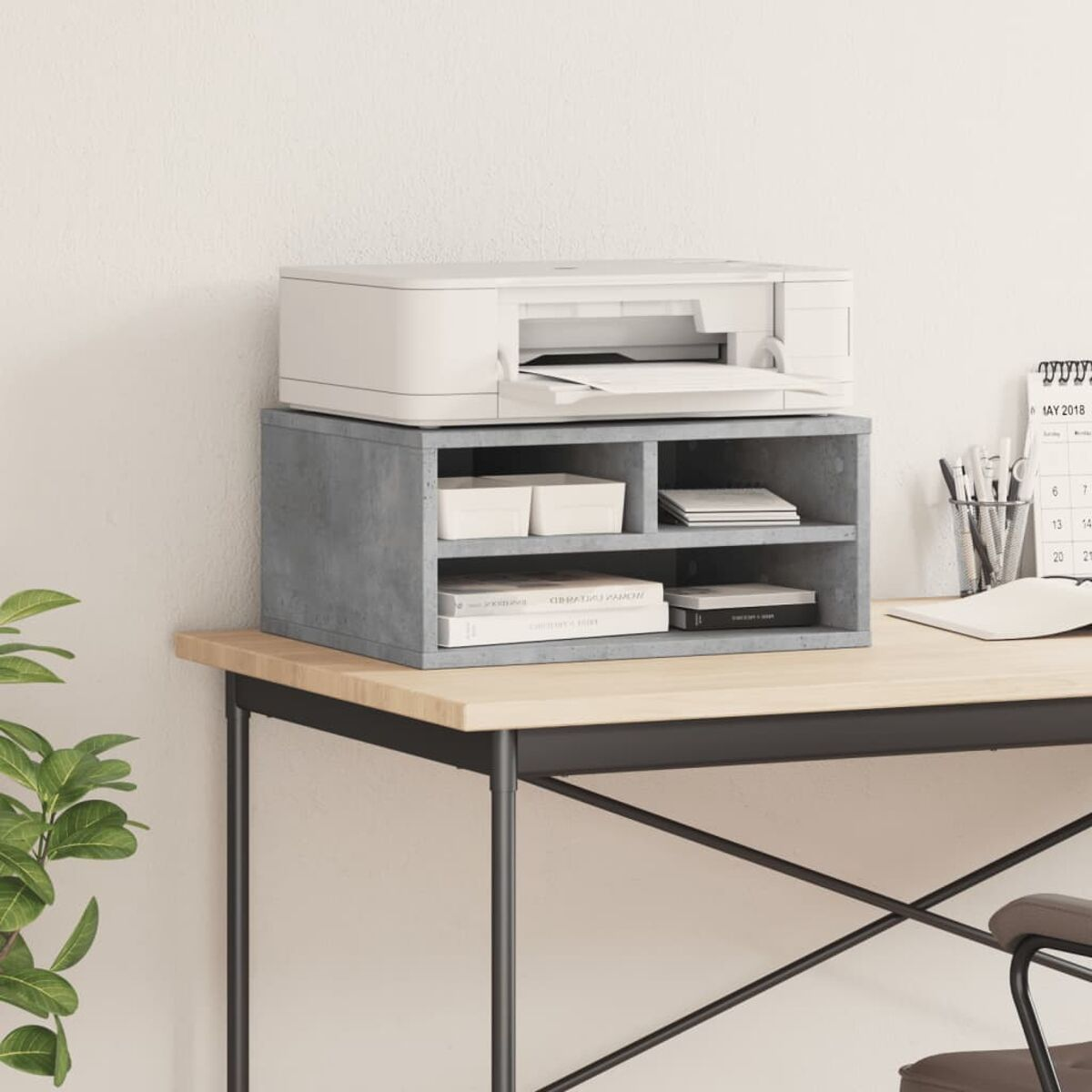 Ein Drucker steht auf einem grauen Regal mit Büchern und Boxen. Daneben ein Kalender.