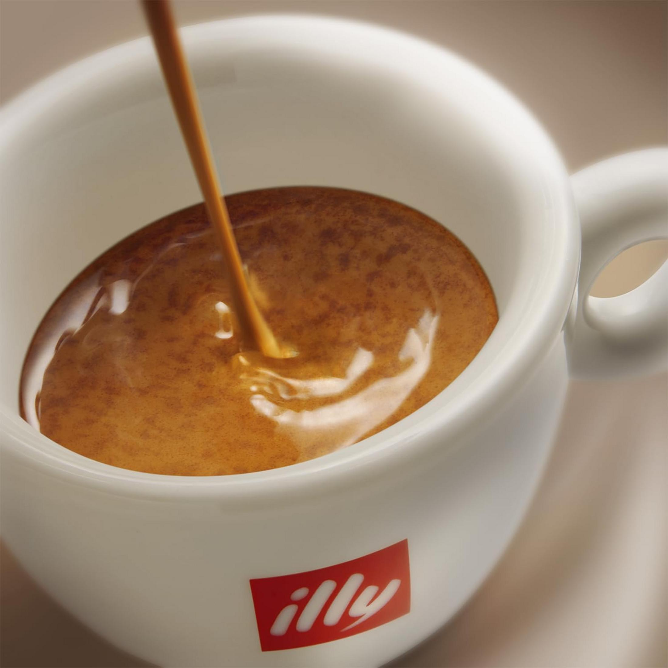L'espresso viene versato in una tazza bianca con il logo Illy.