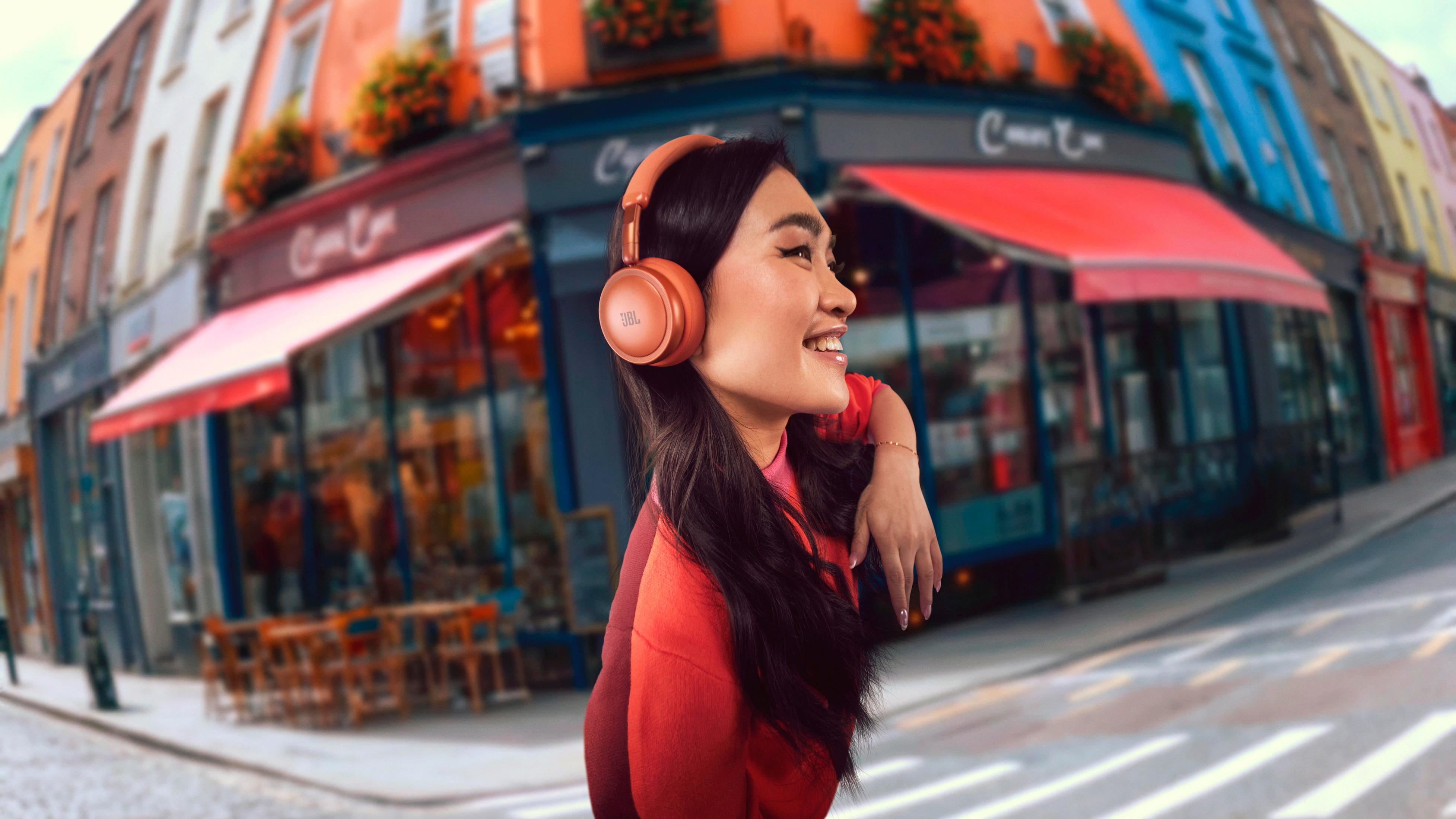 Donna con cuffie arancioni sorride in una strada con edifici colorati.