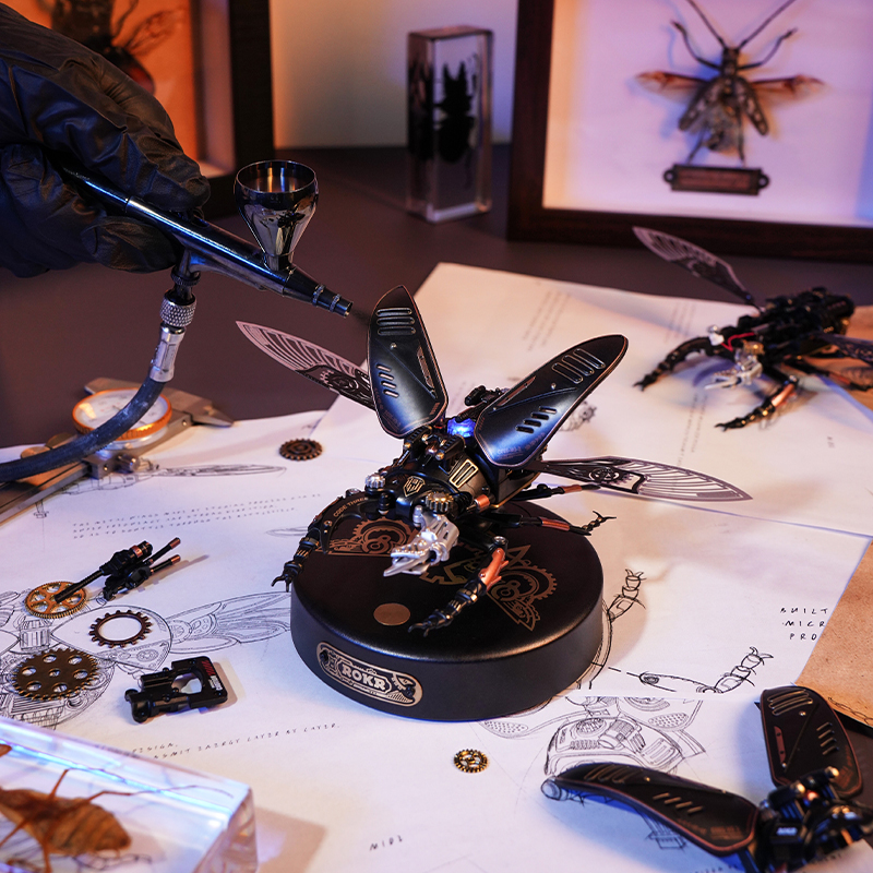 Mavi baskılar üzerinde steampunk böcek modeli. El yakında bir airbrush tutuyor.